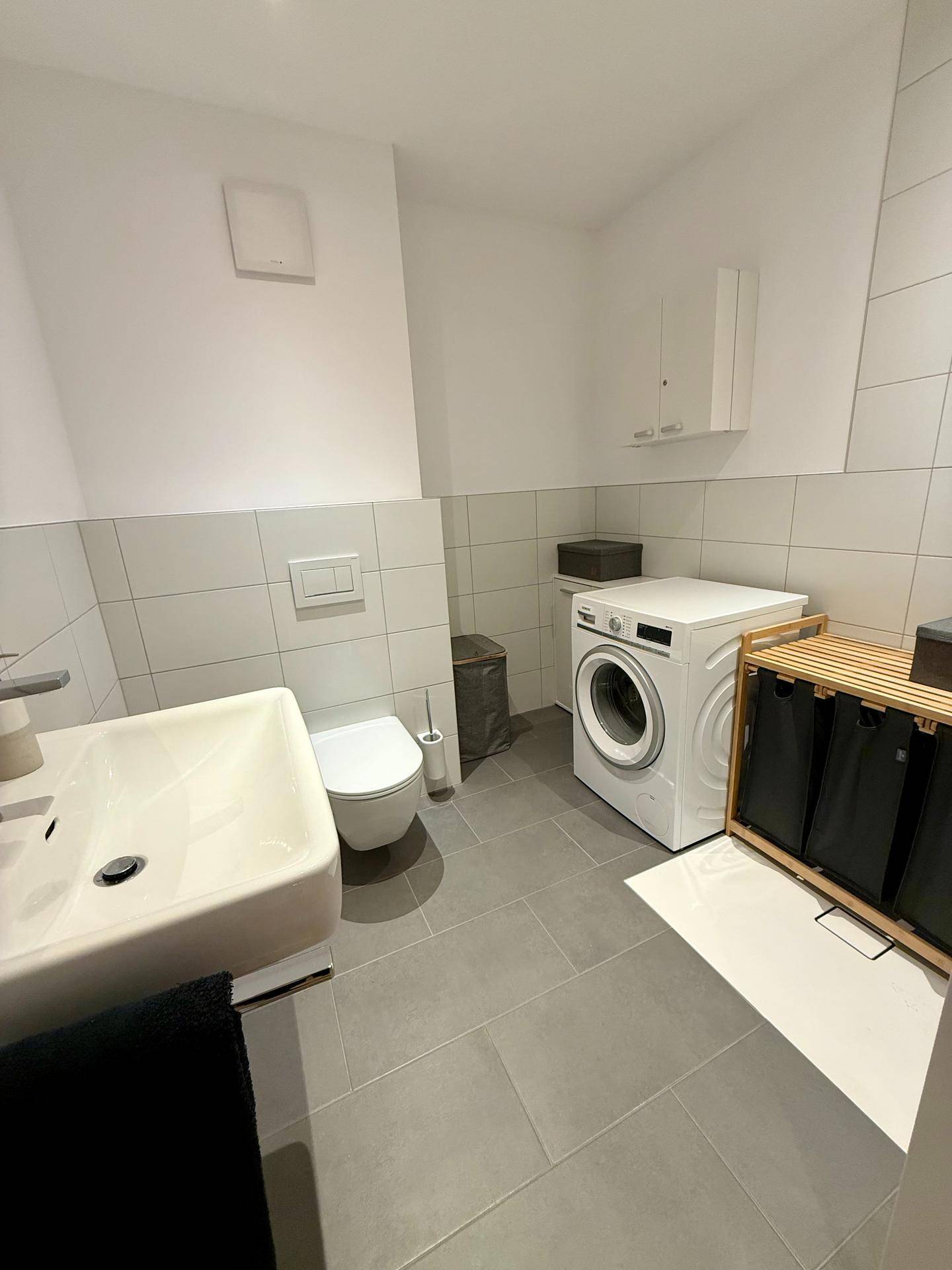 Kleines Badezimmer mit Waschbecken, Toilette und Waschmaschine, praktisch eingerichtet.