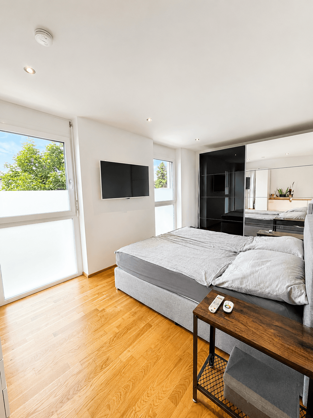 Helles Schlafzimmer mit Holzboden, großem Bett, Wandfernseher und Spiegelschränken.