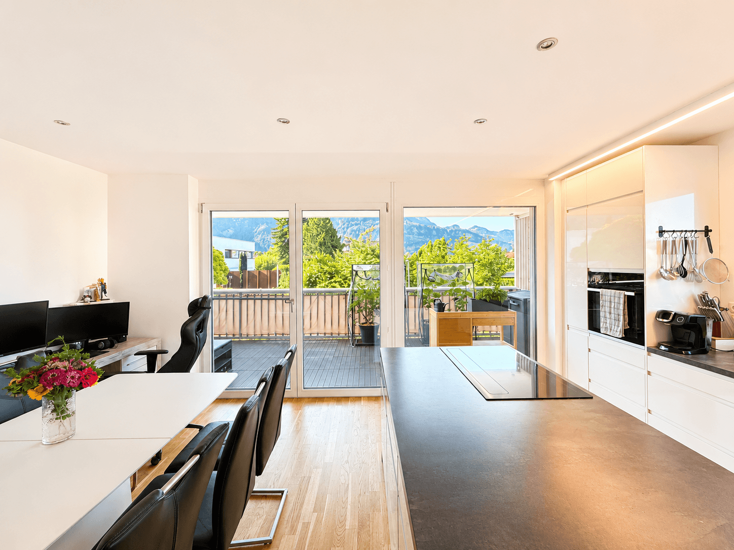 Moderne Kücheninsel mit Induktionskochfeld und Essbereich, mit Blick auf die Berge und den Balkon.