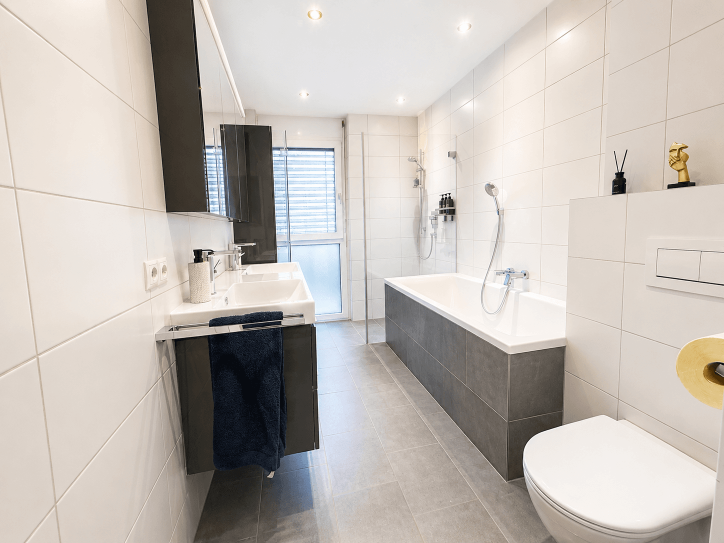 Modernes Badezimmer mit Doppelwaschbecken, Badewanne und Duschbereich, hell gefliest.