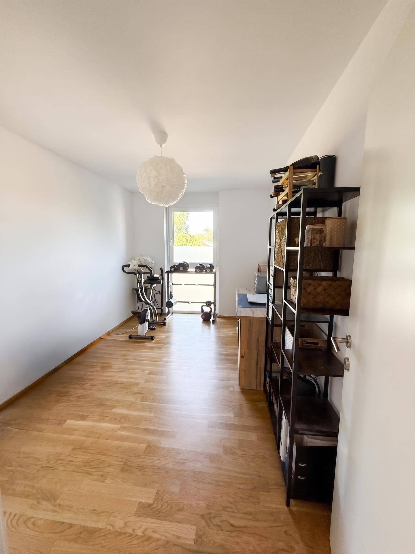 Vielseitiger Raum mit Holzboden, genutzt als Büro und Fitnessbereich mit Sportgeräten.