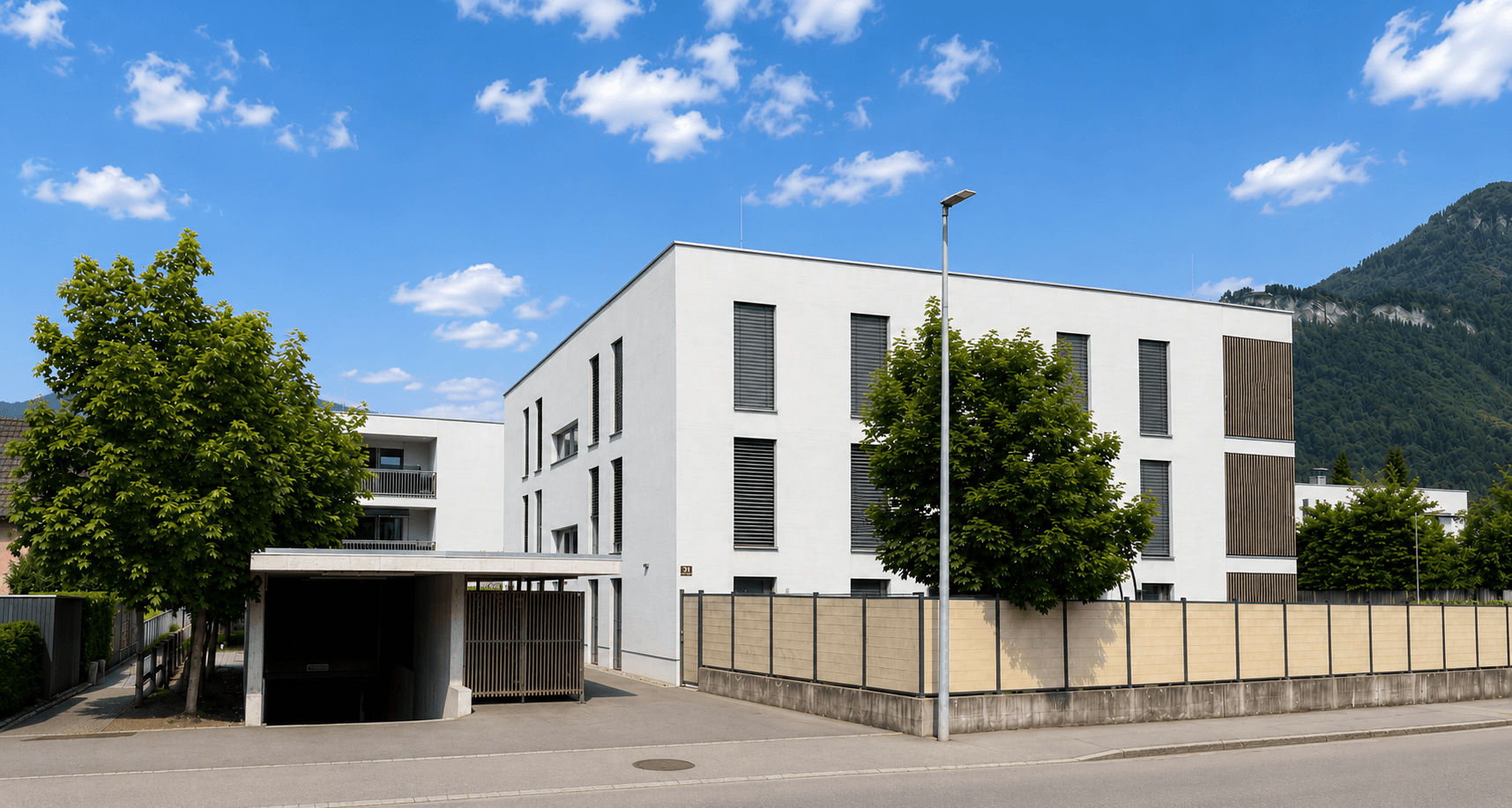 Modernes Mehrfamilienhaus mit klaren Linien, Carport und Bergblick in einer grünen Umgebung.