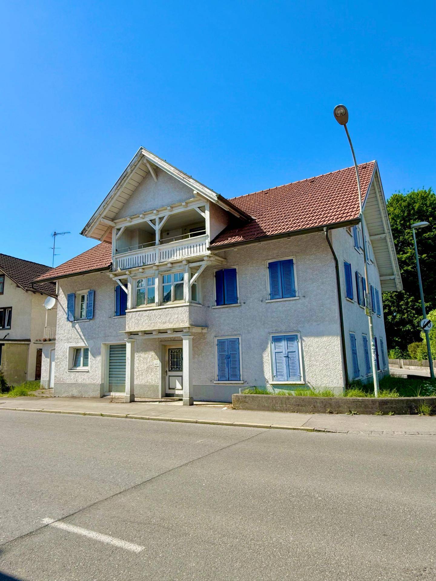 Seitenansicht des Wohnhauses mit markantem Giebel, Balkon und blauen Fensterläden an einem sonnigen Tag.