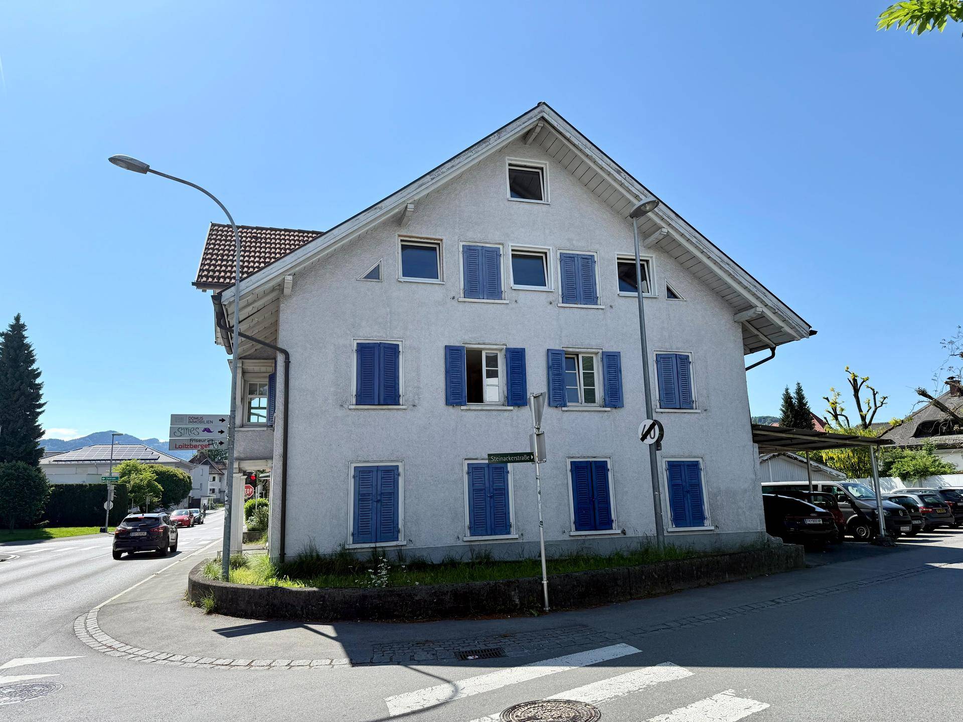 Rückansicht des Wohnhauses mit vielen blauen Fensterläden und Blick auf die umliegende Straße.
