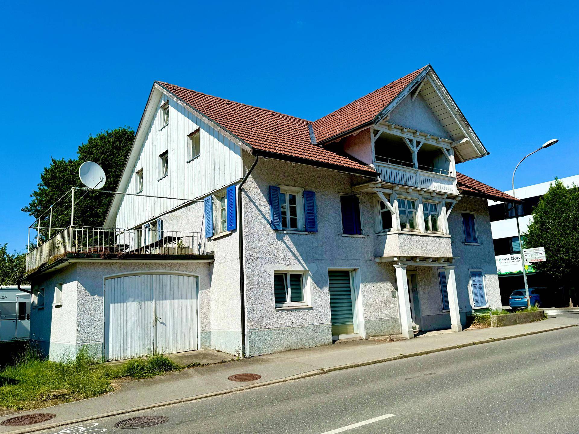 Historisches Wohnhaus mit blauen Fensterläden, Garage und Balkon unter strahlend blauem Himmel.
