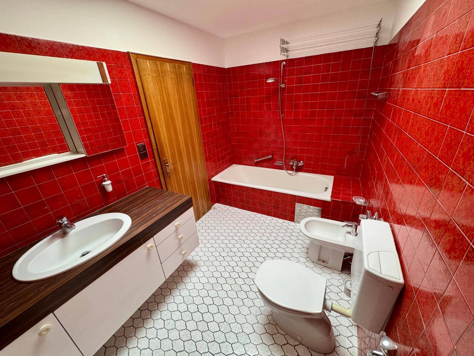 Badezimmer mit roten Fliesen, Badewanne, Bidet und Einzelwaschbecken mit Holzunterschrank.