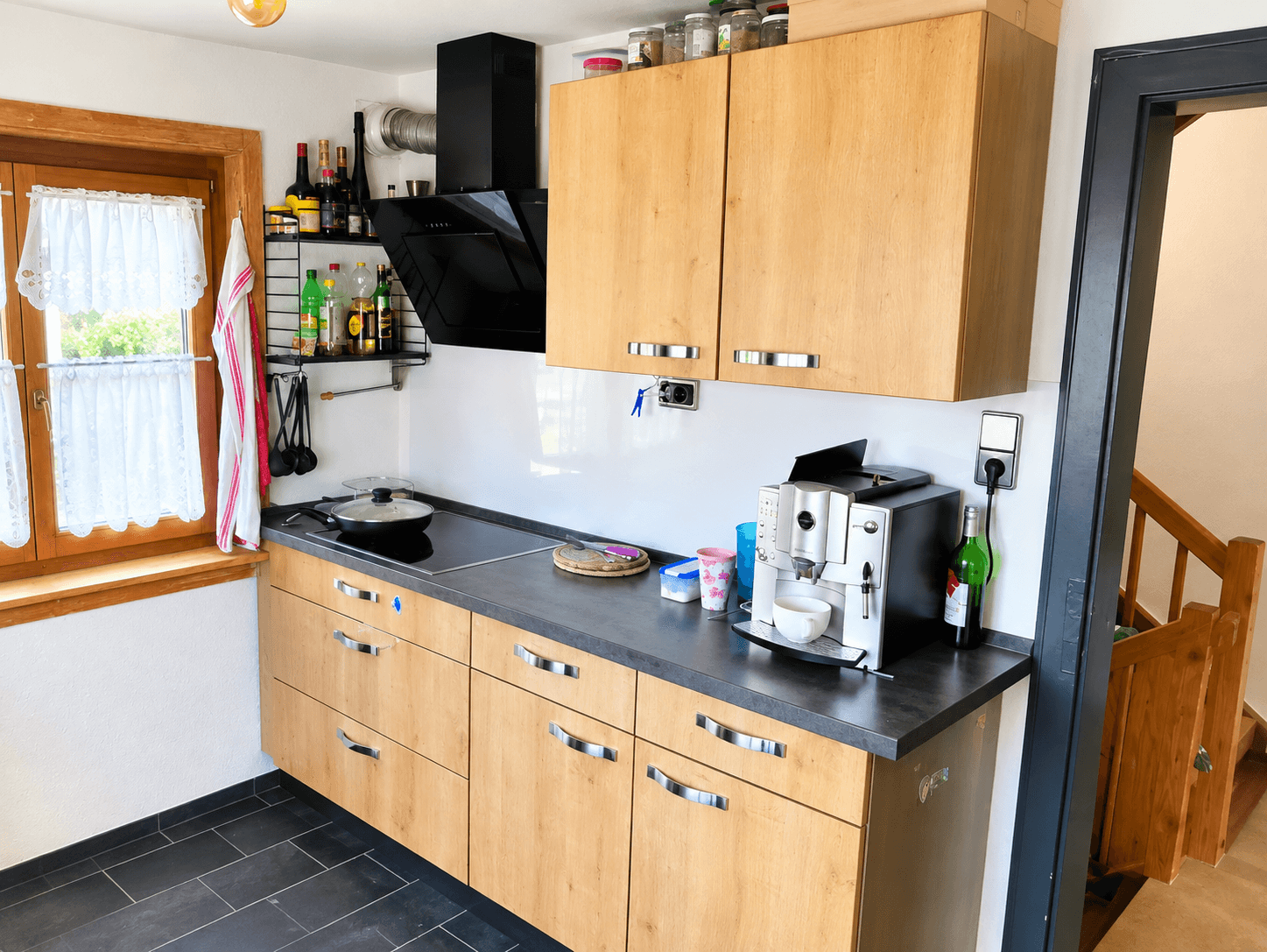 Moderne Küche mit Holzschränken, dunkler Arbeitsplatte und Kaffeemaschine.