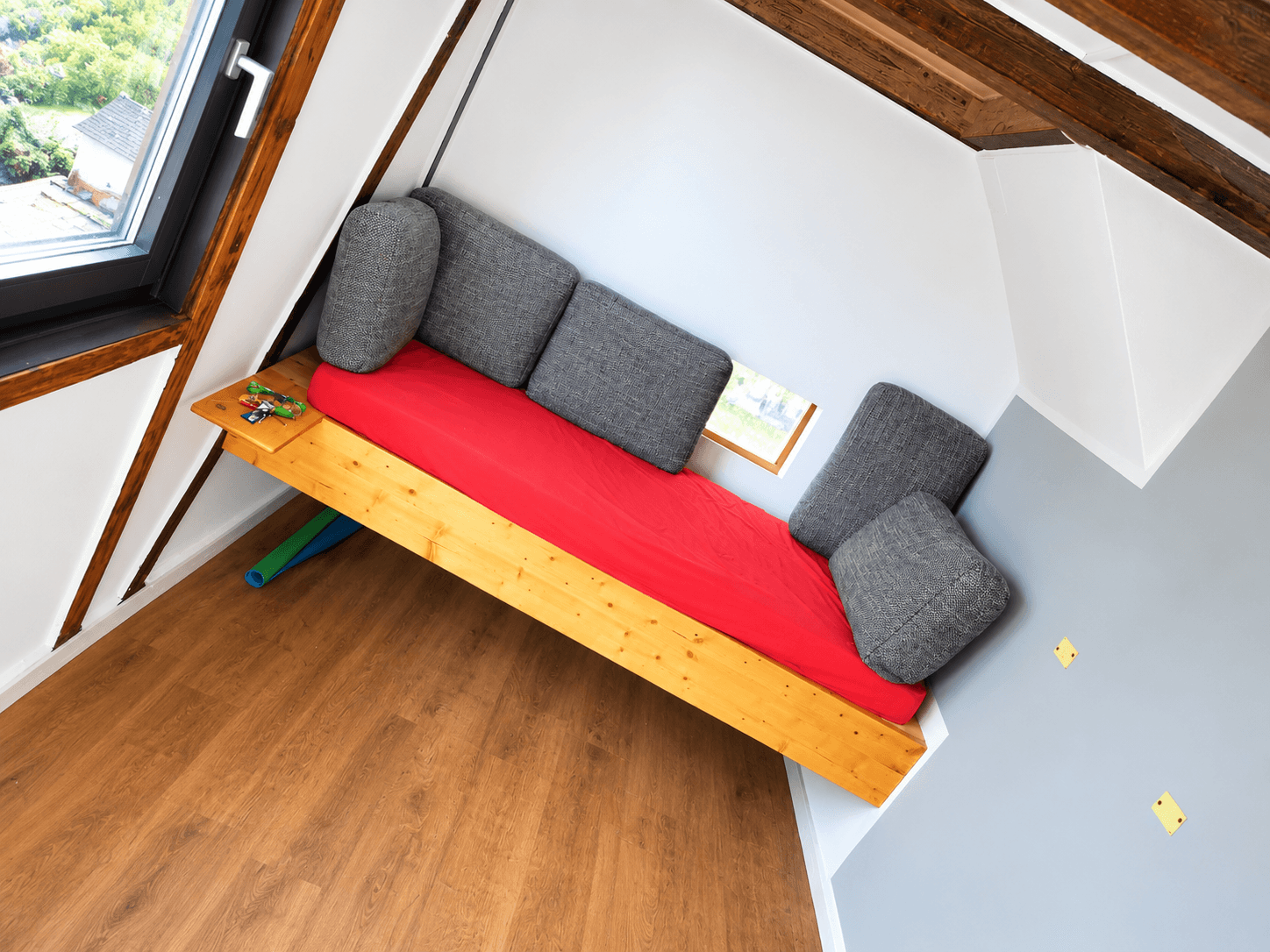 Gemütlicher Schlafbereich unter dem Dach mit Holzbalken und Dachfenster.