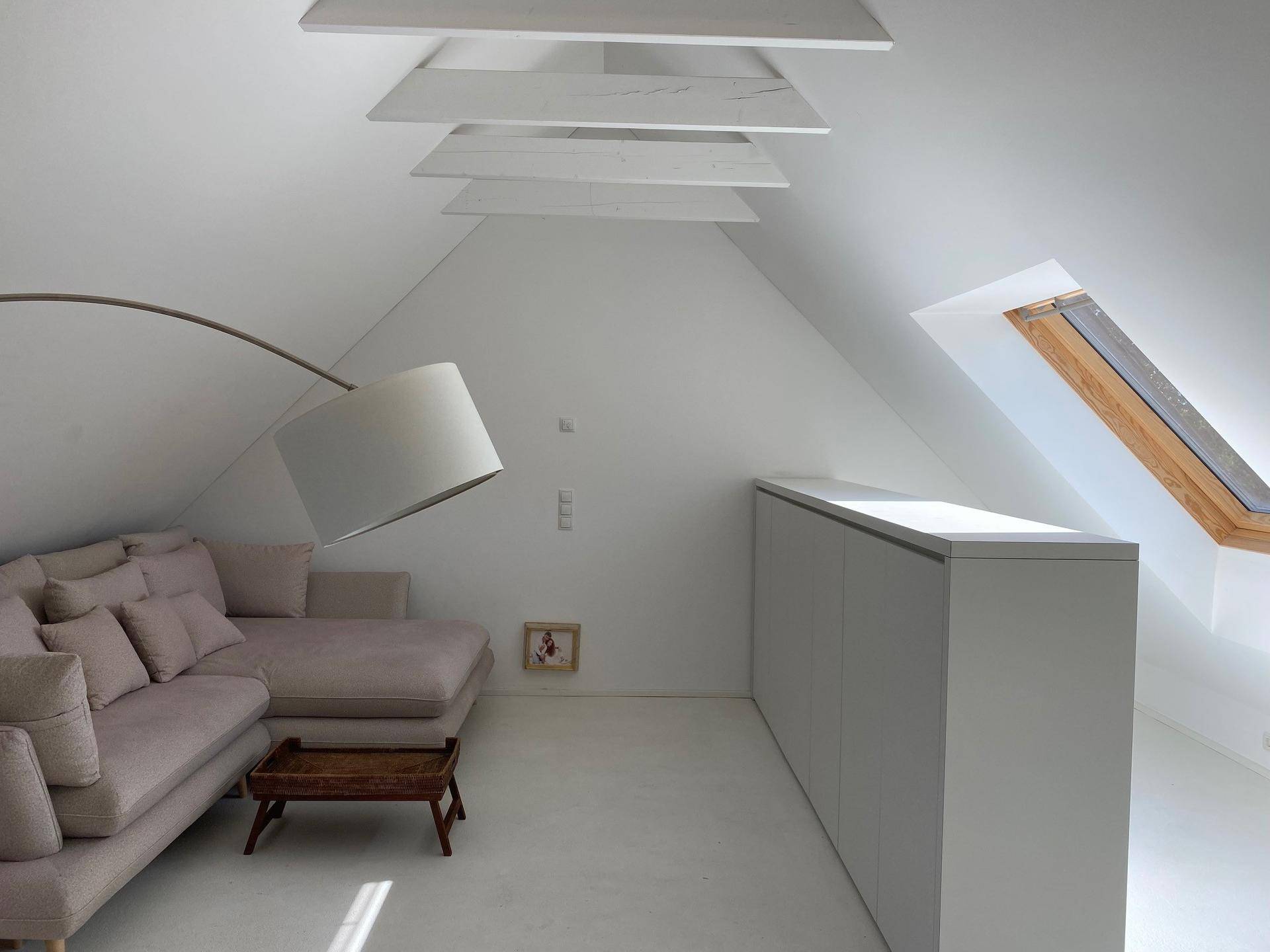 Gemütlicher Wohnbereich im Dachgeschoss mit schrägen Wänden, Sofa und Dachfenster für Helligkeit.