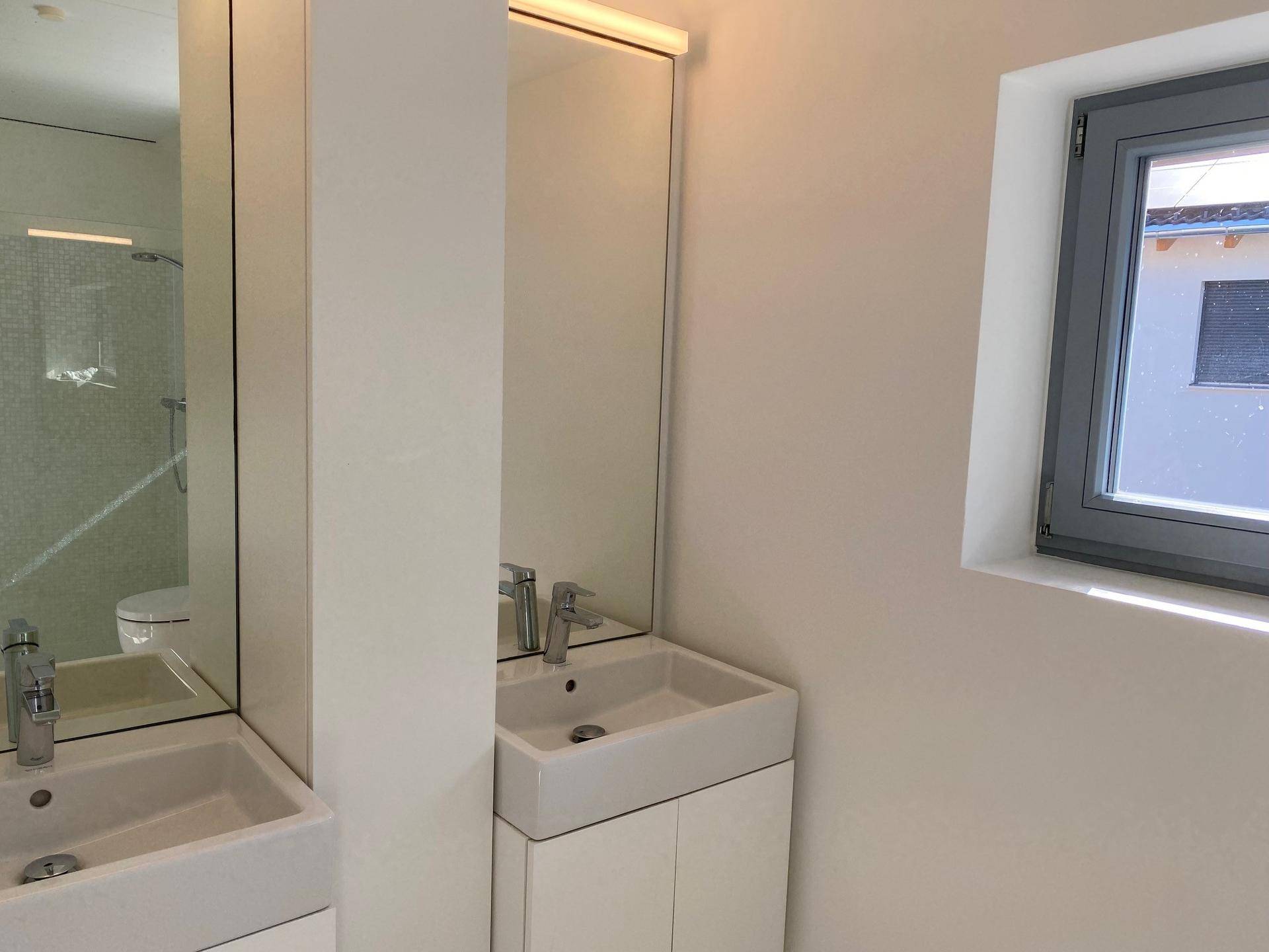 Helles Badezimmer mit zwei Waschbecken, Spiegelschränken und einem Fenster für natürliche Belüftung.