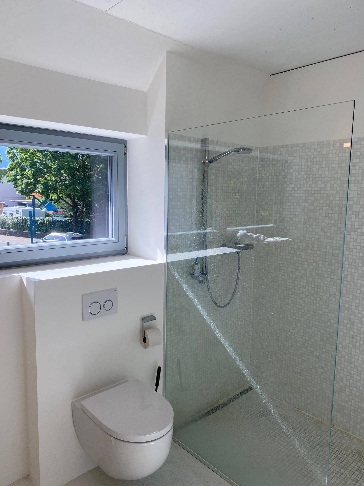 Modernes Badezimmer mit bodengleicher Dusche, wandhängendem WC und Fenster für Tageslicht.