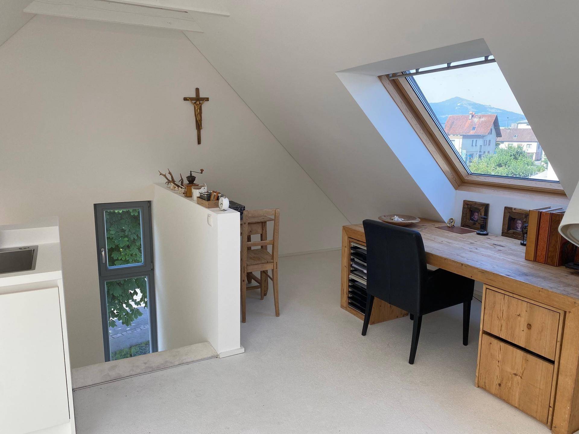 Helles Dachgeschoss-Büro mit Holztisch, Dachfenster und Blick auf die umliegende Landschaft.