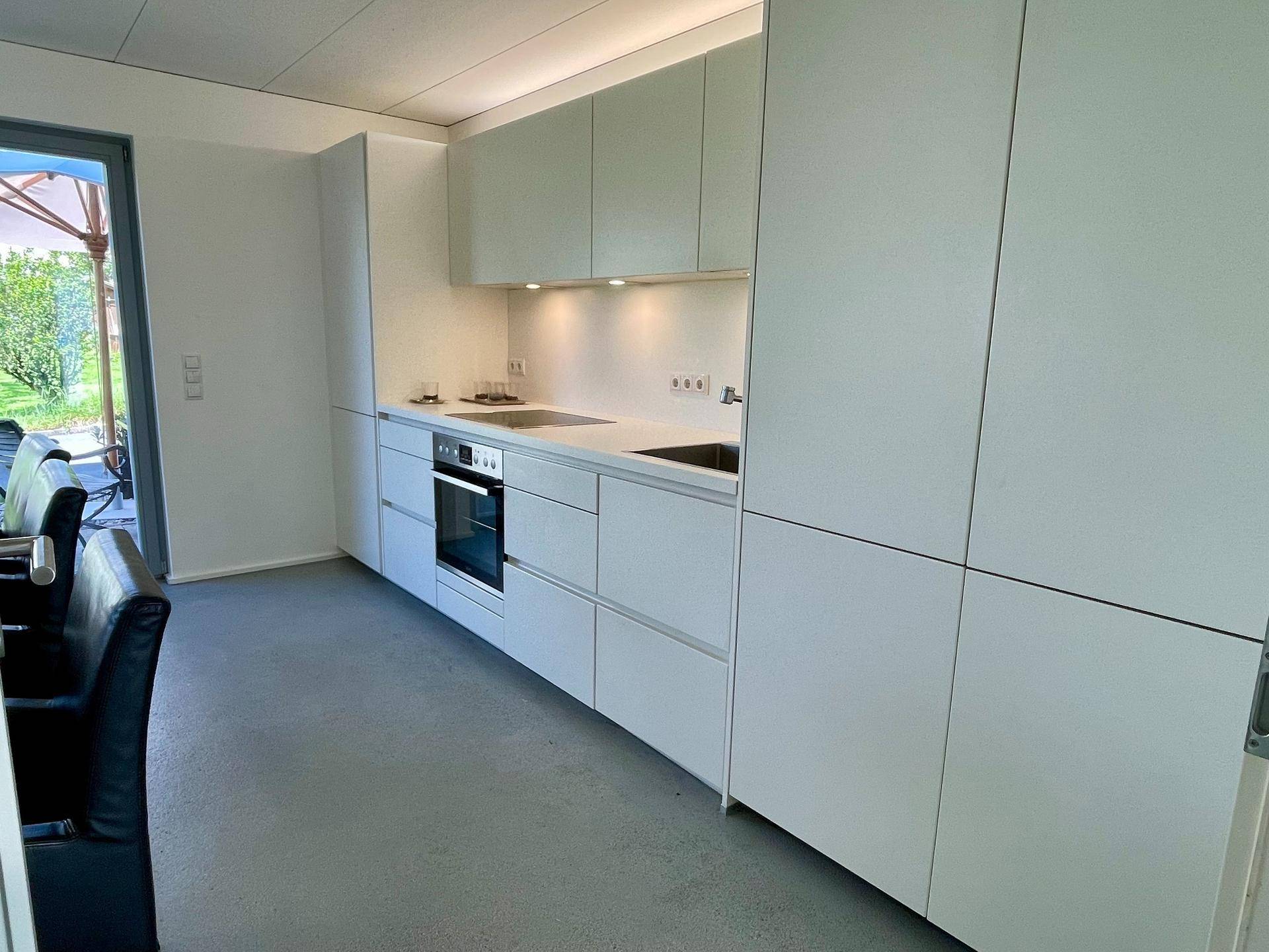 Moderne, minimalistische Küche mit weißen Schränken, integrierten Geräten und Zugang zur Terrasse.