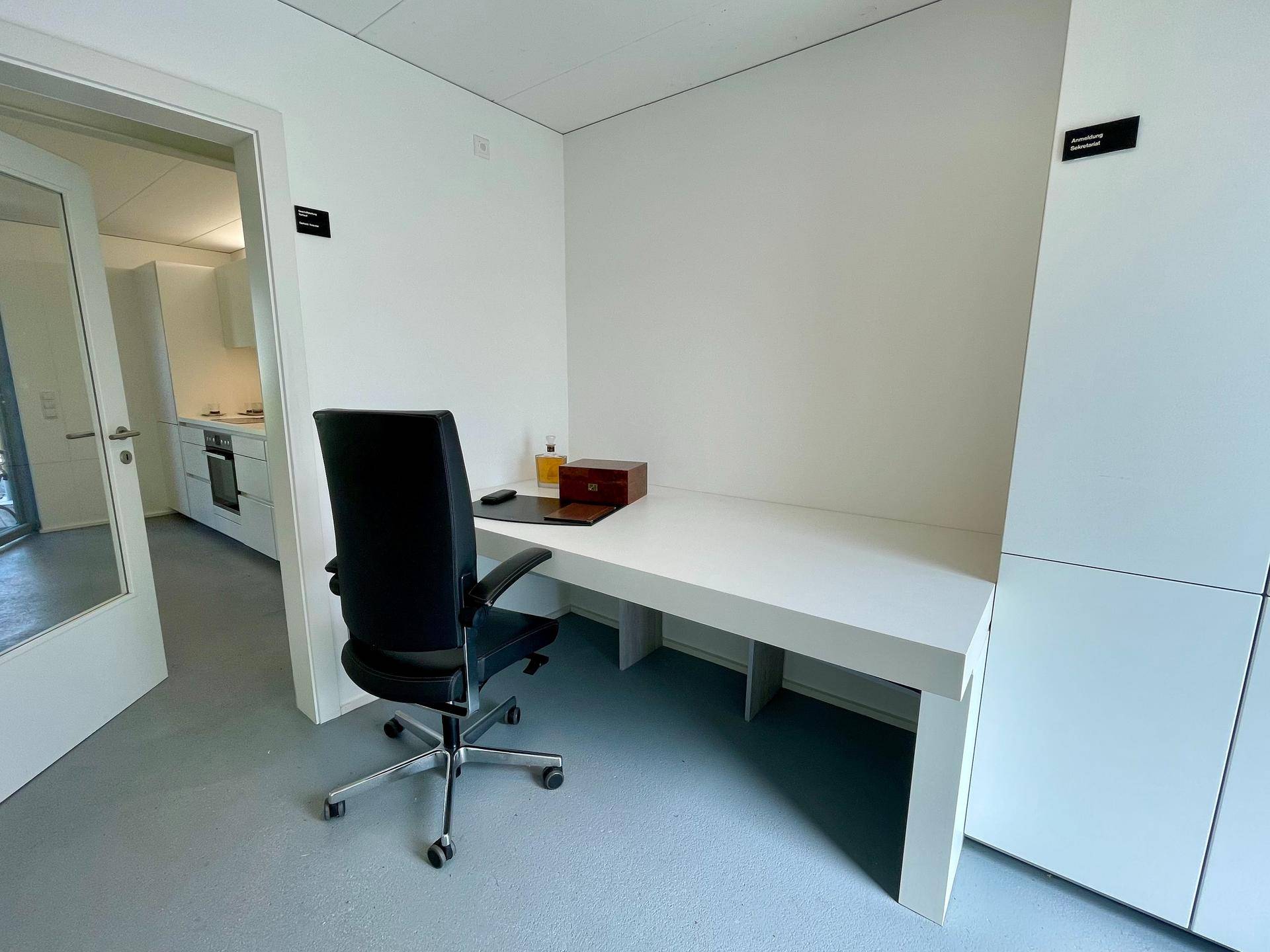 Funktionaler Arbeitsbereich mit weißem Schreibtisch und Blick in eine angrenzende moderne Küche.