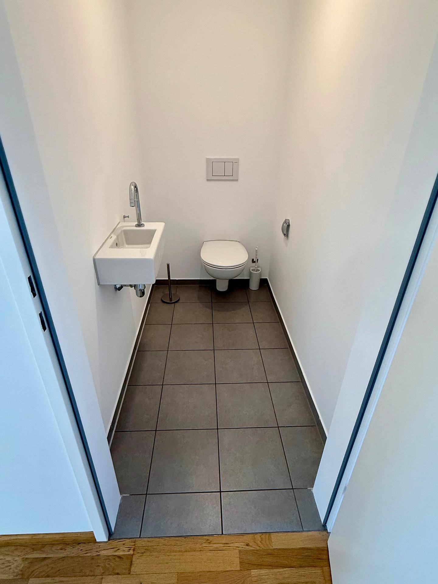 Kleines Gäste-WC mit Wand-WC, Handwaschbecken und modernen grauen Bodenfliesen.