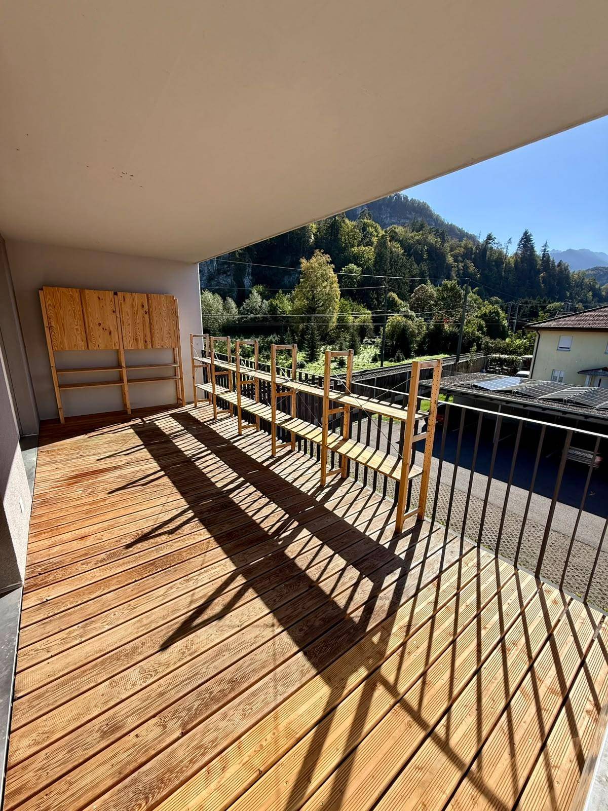 Sonniger Balkon mit Holzfußboden, Regalen und einem weiten Blick auf die grüne Berglandschaft.