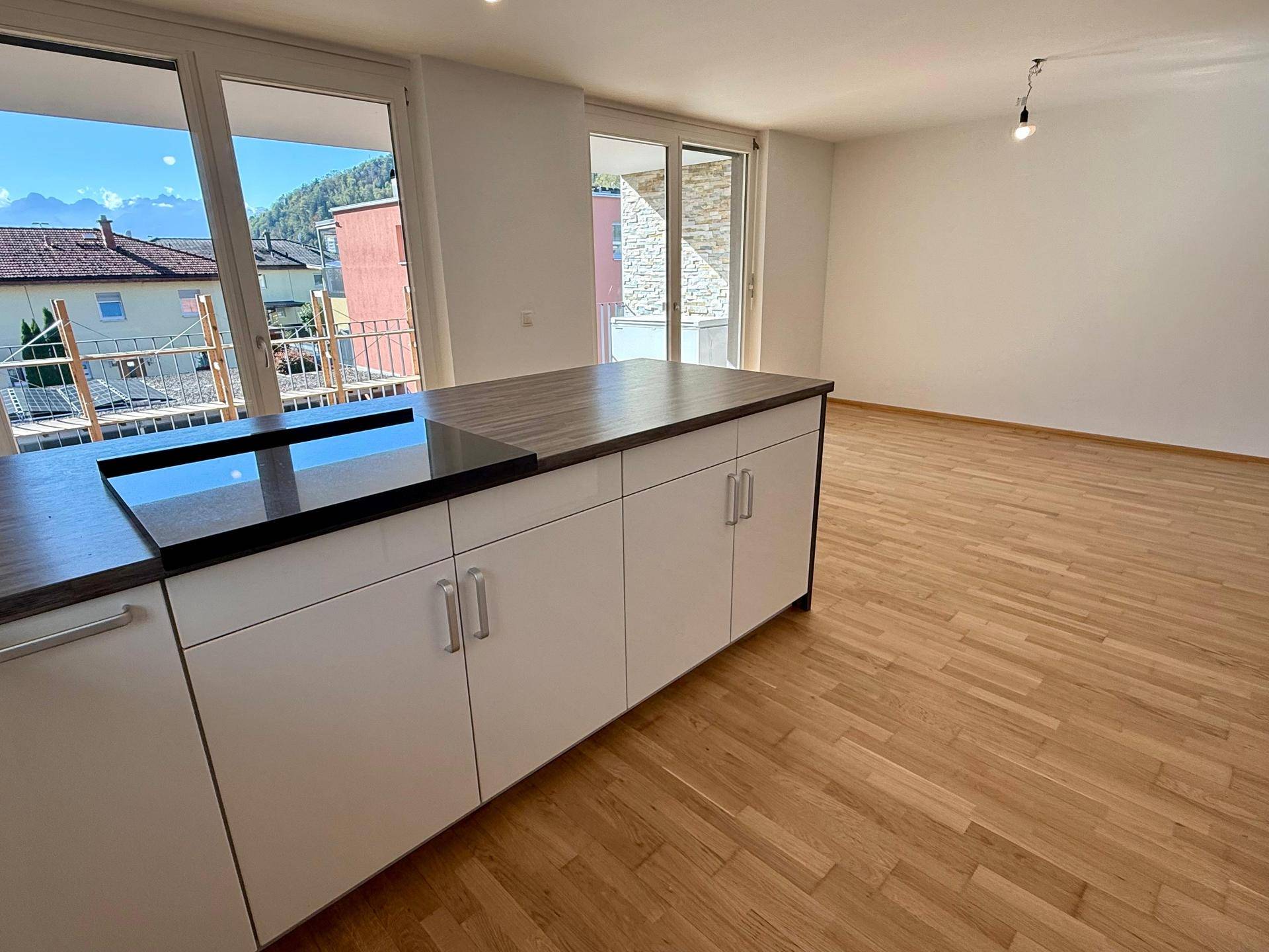 Offener Wohnbereich mit Kücheninsel, Parkettboden und Zugang zu einem Balkon mit Bergblick.