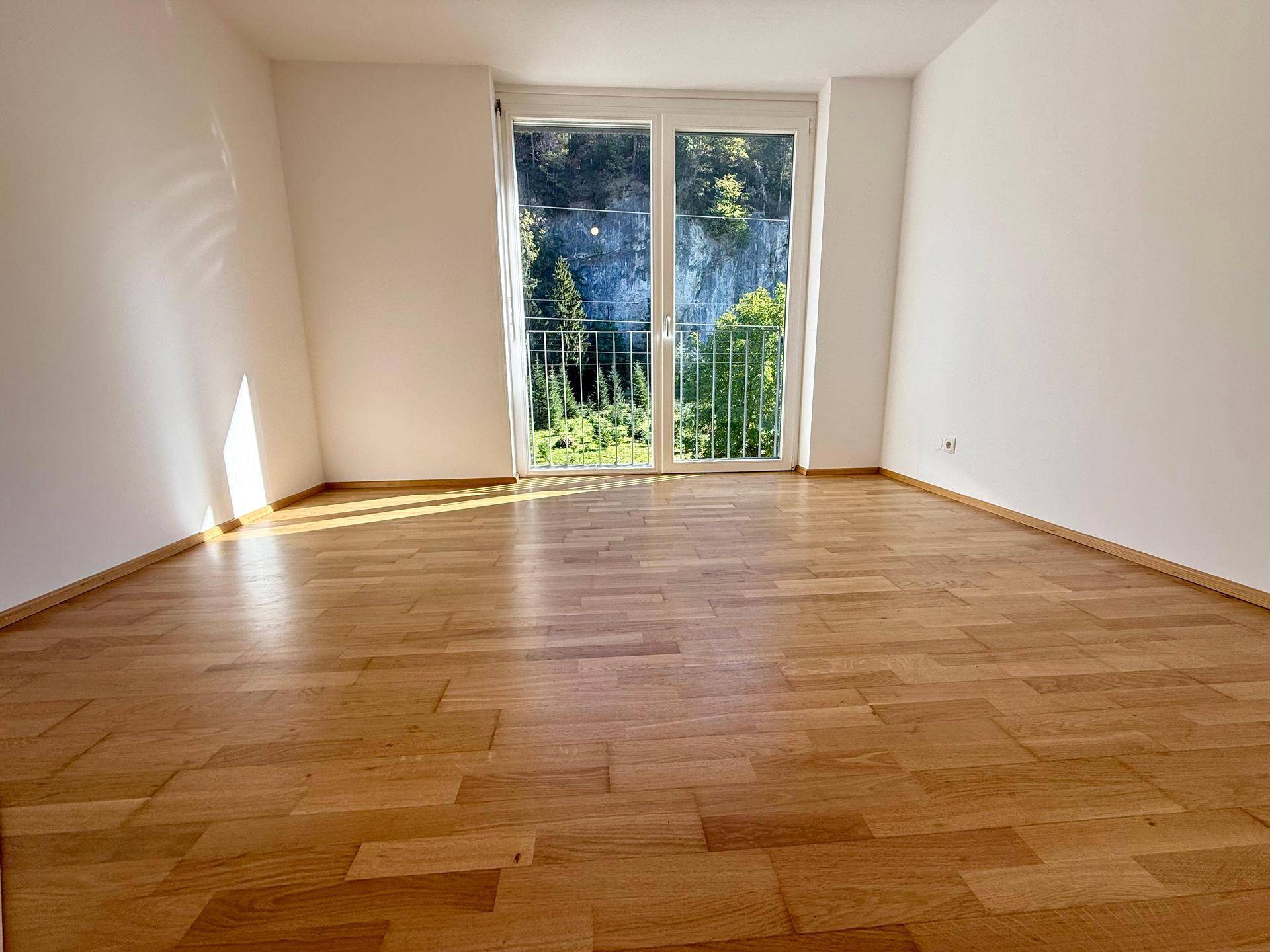 Heller Raum mit Parkettboden, großen Fenstern und einem schönen Blick auf die umliegenden Berge.