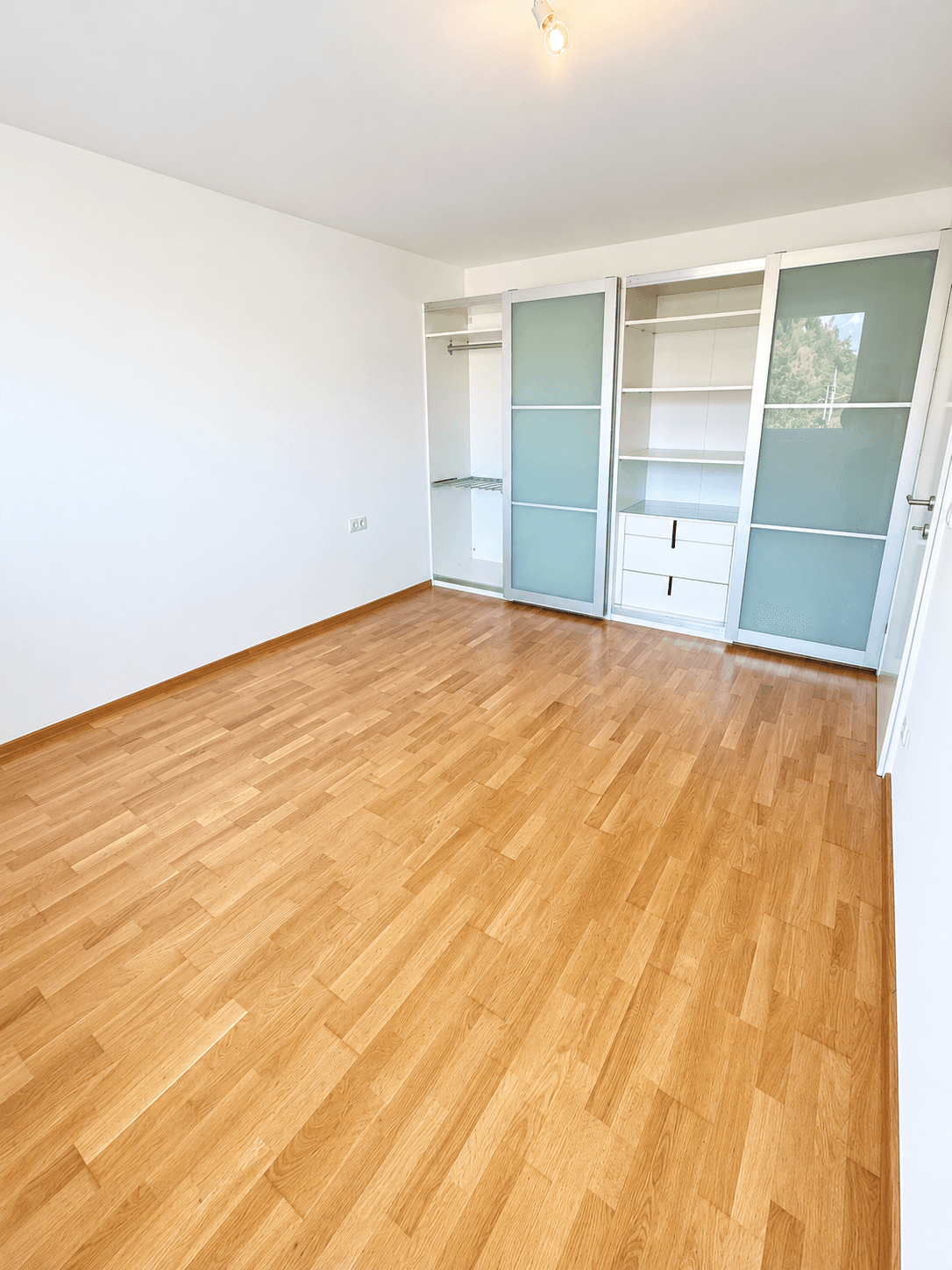 Leeres Zimmer mit hellem Parkettboden und praktischem Einbauschrank mit Schiebetüren.