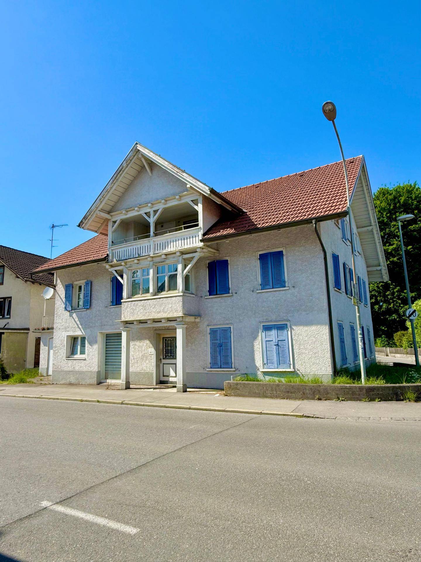 Schrägansicht des Wohnhauses mit traditioneller Architektur, roten Dachziegeln und blauen Fensterläden.