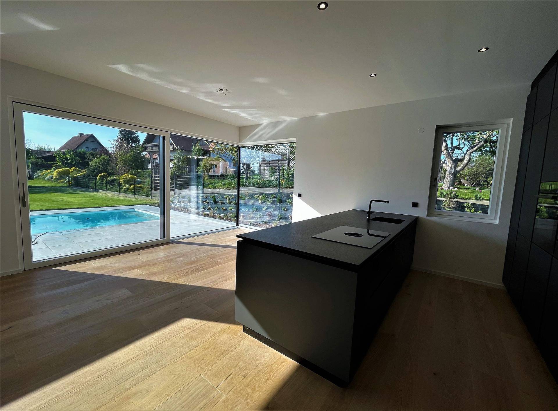 Moderne Küche mit Kochinsel und großzügigen Fenstern, die den Blick auf den Pool freigeben.