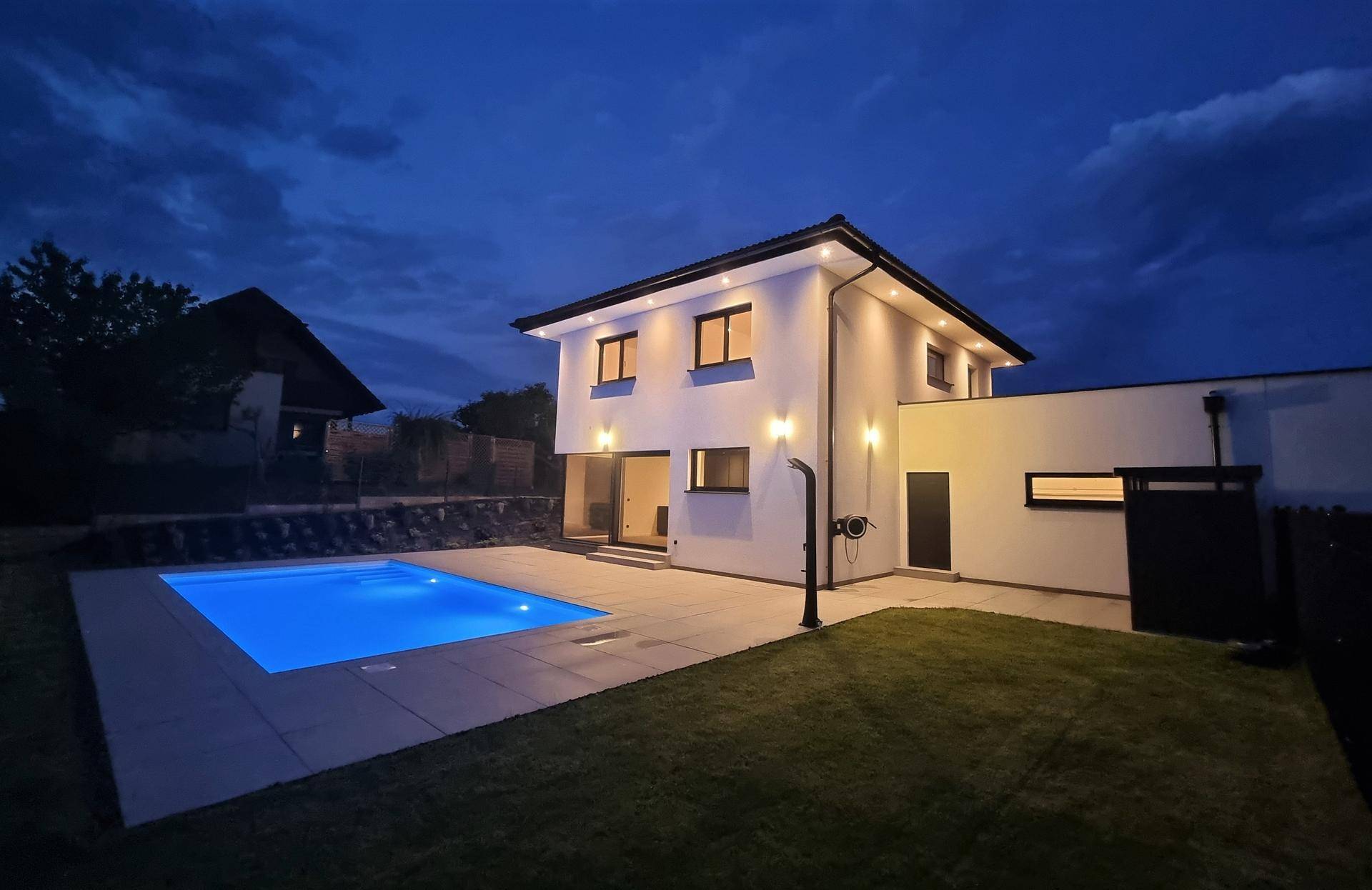 Modernes Haus mit beleuchtetem Pool und Garten bei Einbruch der Dunkelheit.