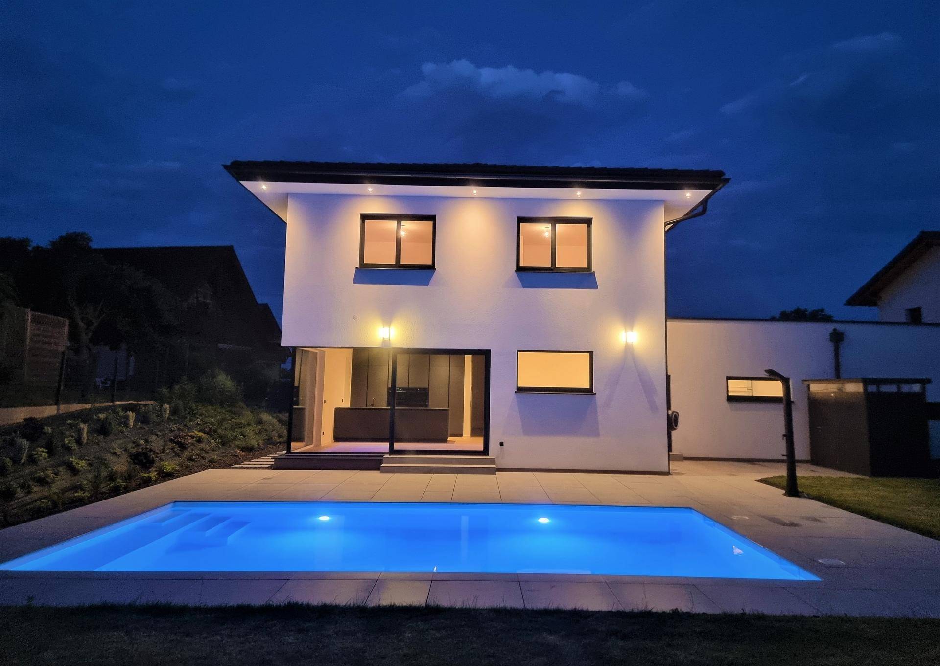 Beleuchtetes Einfamilienhaus mit Pool und Terrasse in der Abenddämmerung.