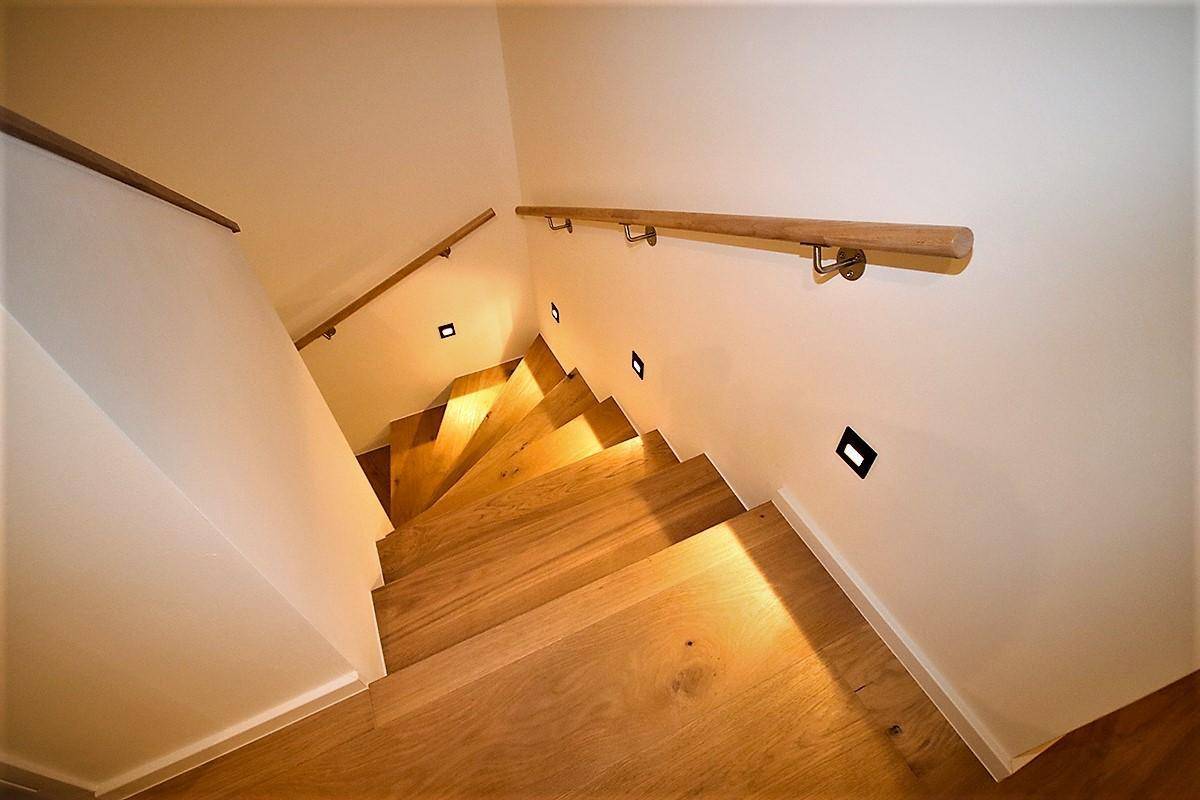 Elegante Holztreppe mit integrierter Beleuchtung und Holzhandläufen, die die Etagen verbindet.