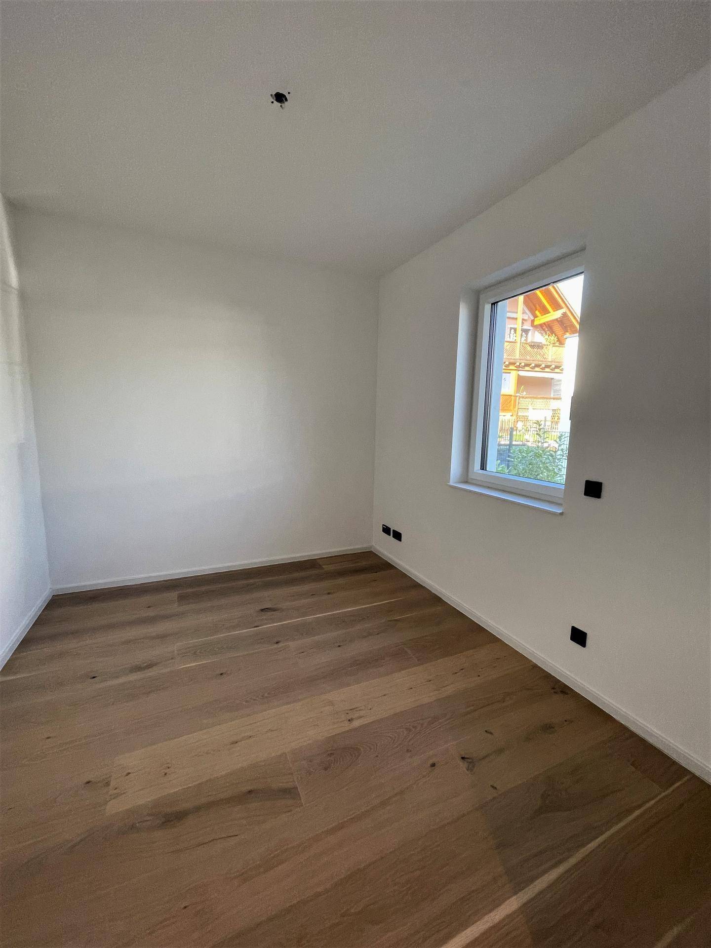 Helles Zimmer mit Holzboden und einem Fenster, das den Blick nach draußen freigibt.