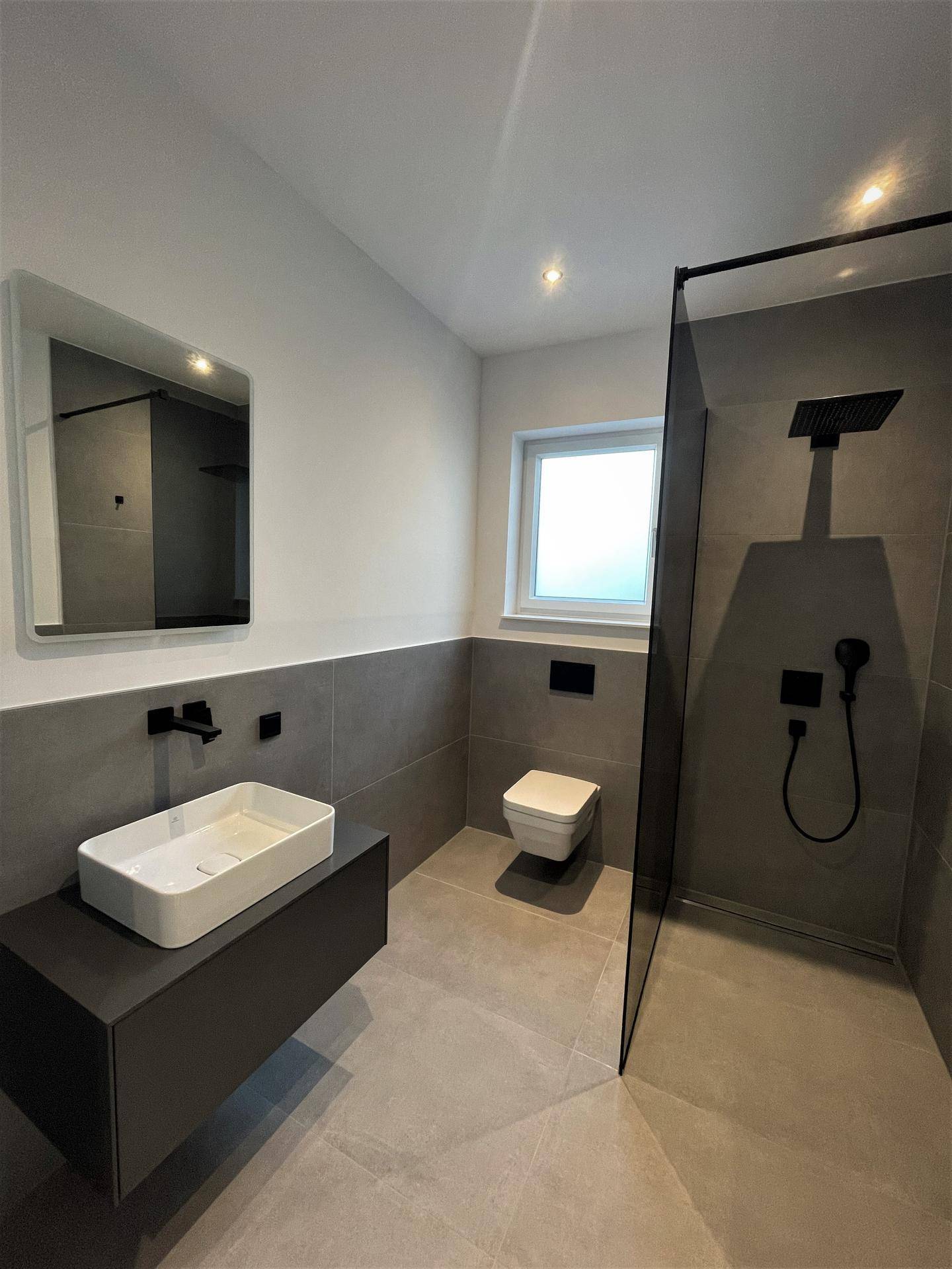 Modernes Badezimmer mit begehbarer Dusche, Wand-WC und eleganten grauen Fliesen.