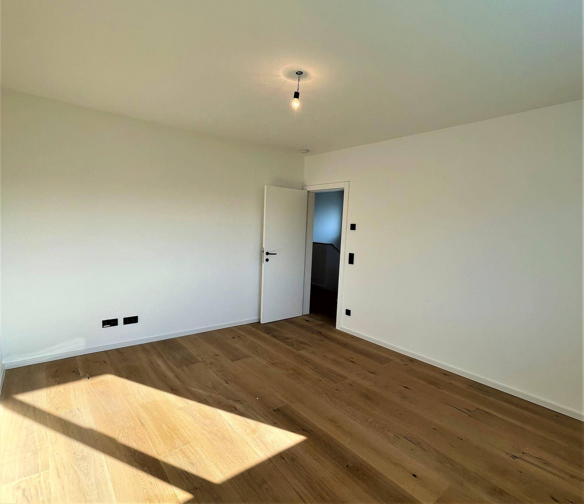Geräumiges, helles Schlafzimmer mit Eichenparkettboden und weiß gestrichenen Wänden.