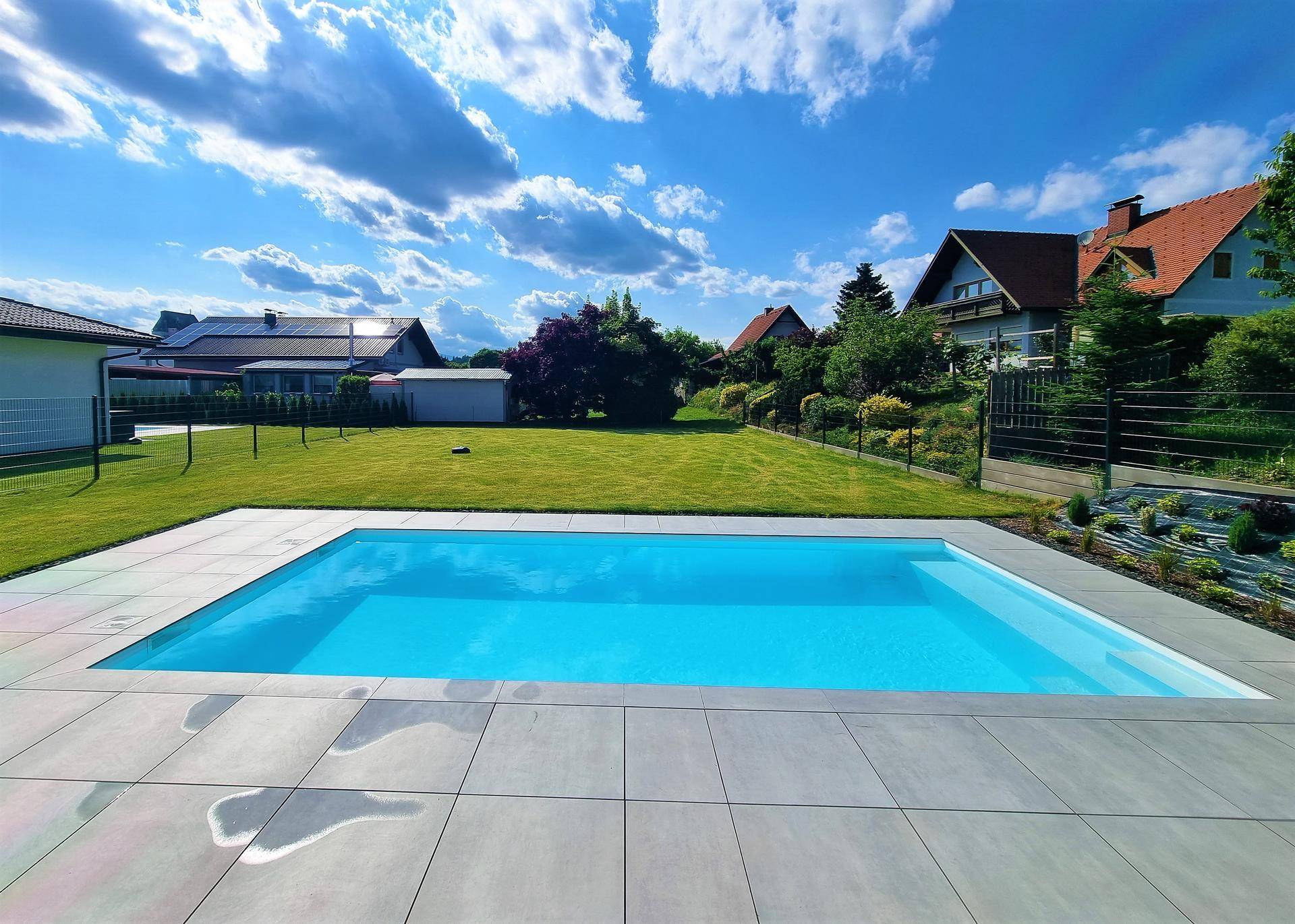 Großzügiger Gartenbereich mit rechteckigem Pool und umliegender Rasenfläche unter blauem Himmel.