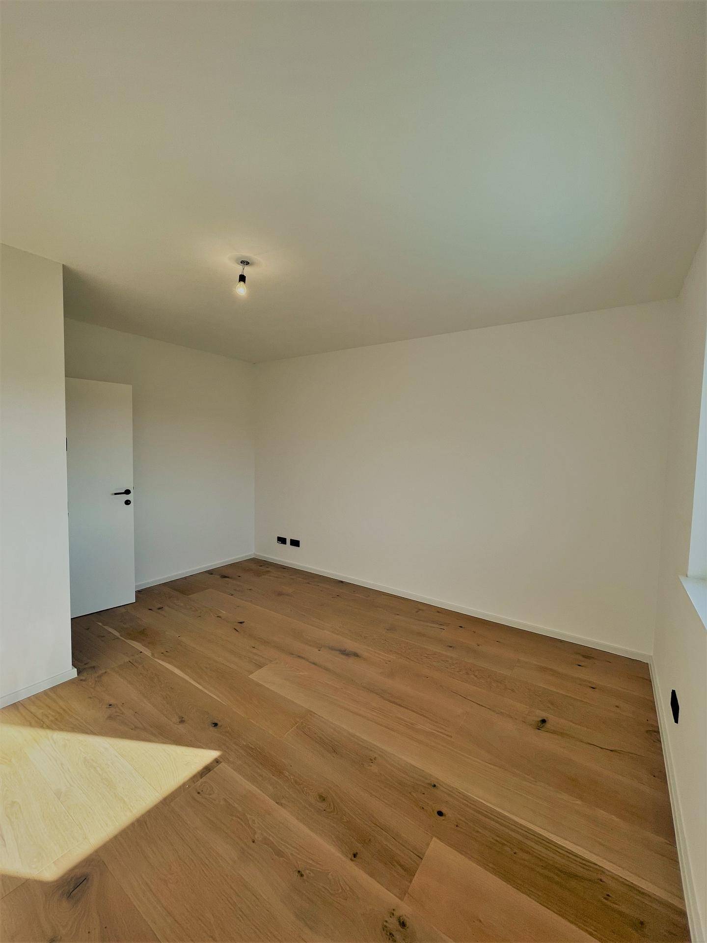 Großes, helles Schlafzimmer mit Eichenparkettboden und schlichten weißen Wänden.