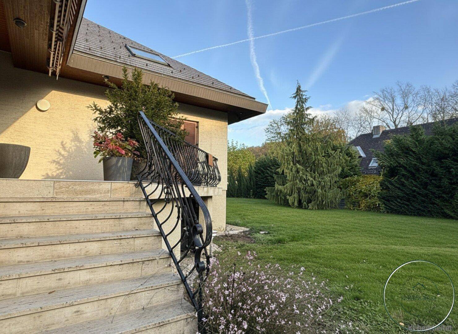 Gepflegter Garten mit Rasenfläche und Steintreppe, die zum Haus hinaufführt.