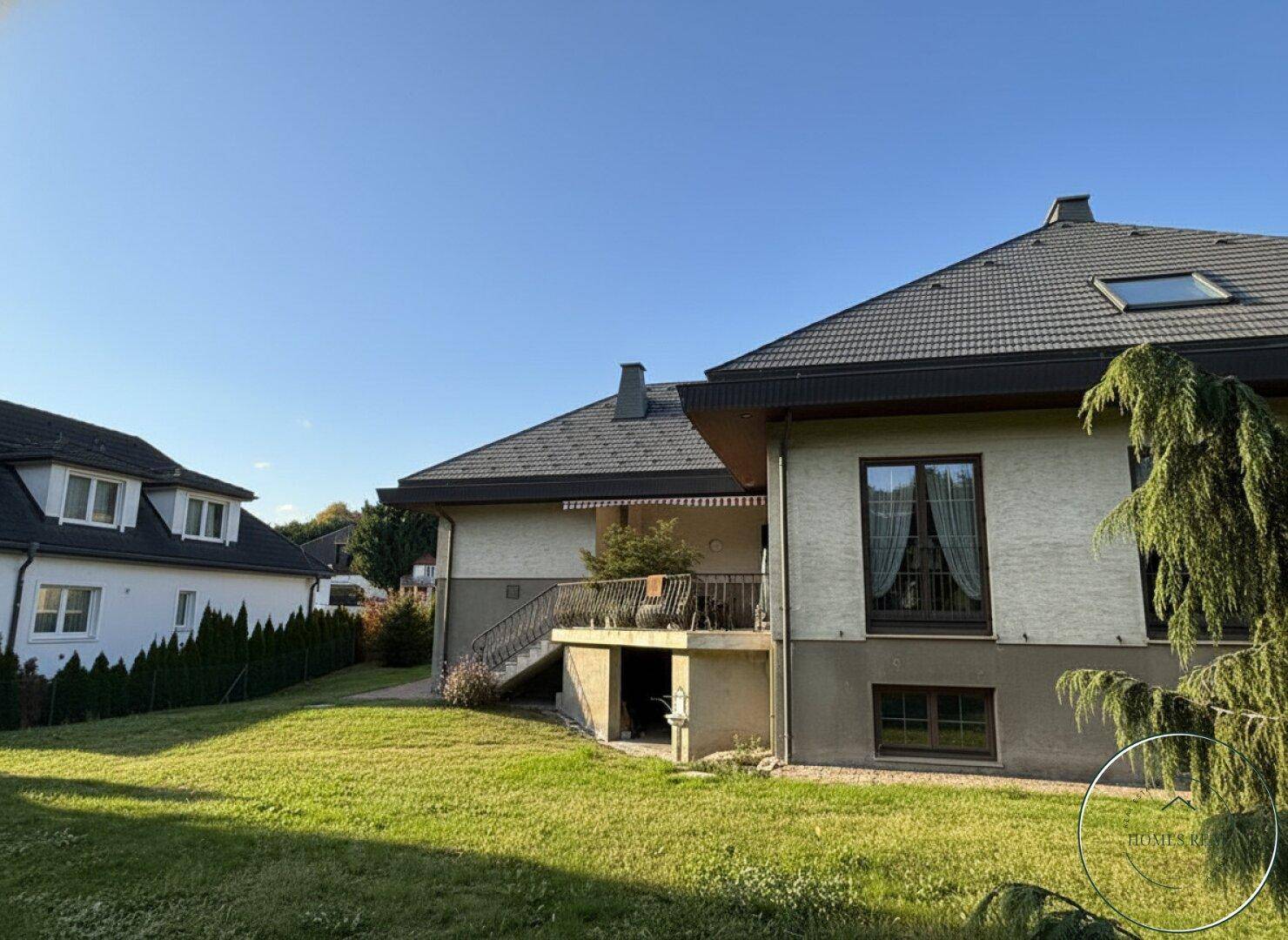 Großzügiger Gartenbereich mit Rasenfläche und Blick auf das Wohnhaus an einem sonnigen Tag.