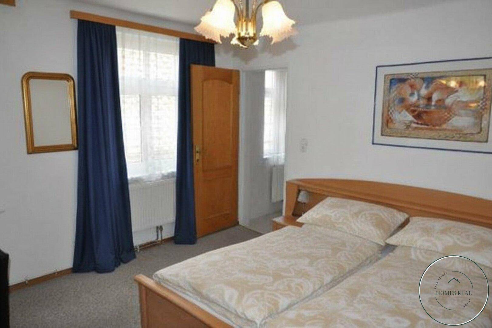 Gemütliches Schlafzimmer mit Holzbetten, blauen Vorhängen und einem klassischen Kronleuchter.