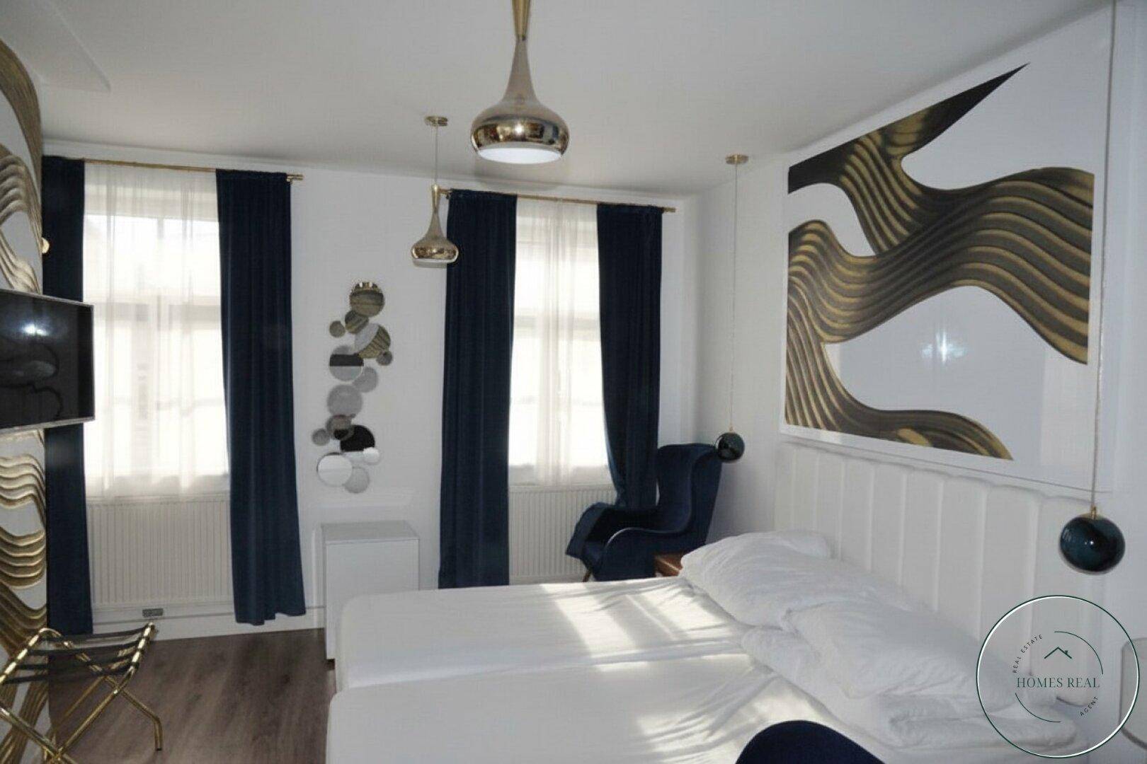 Modern eingerichtetes Schlafzimmer mit zwei Einzelbetten, dunklen Vorhängen und abstrakter Wandkunst.