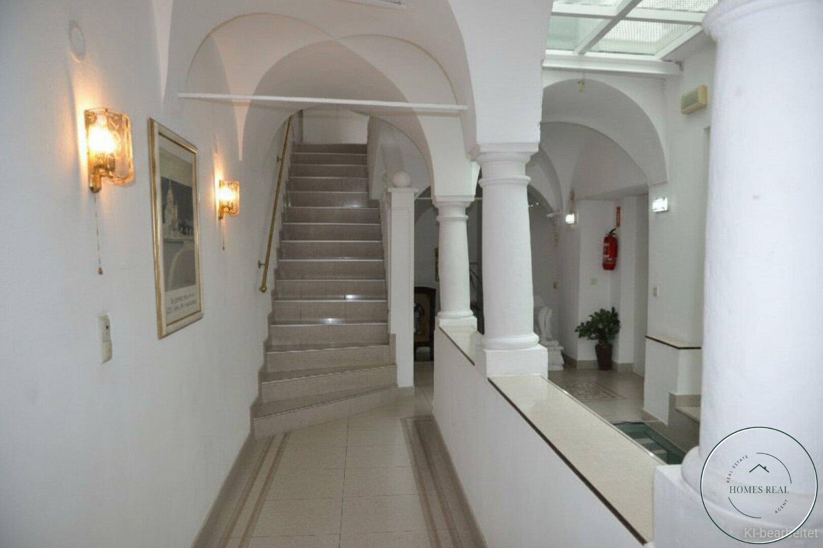 Historischer Flur mit Gewölbedecken, Säulen und einer Treppe, die zu den oberen Etagen führt.