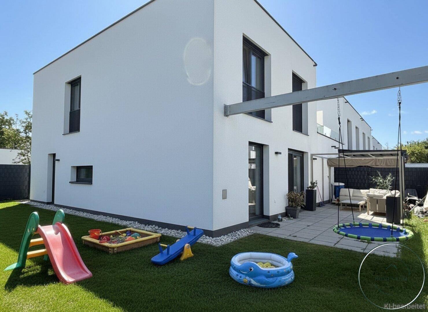 Moderner Neubau mit weißer Fassade, kleinem Garten, Terrasse und Kinderspielgeräten im Freien.