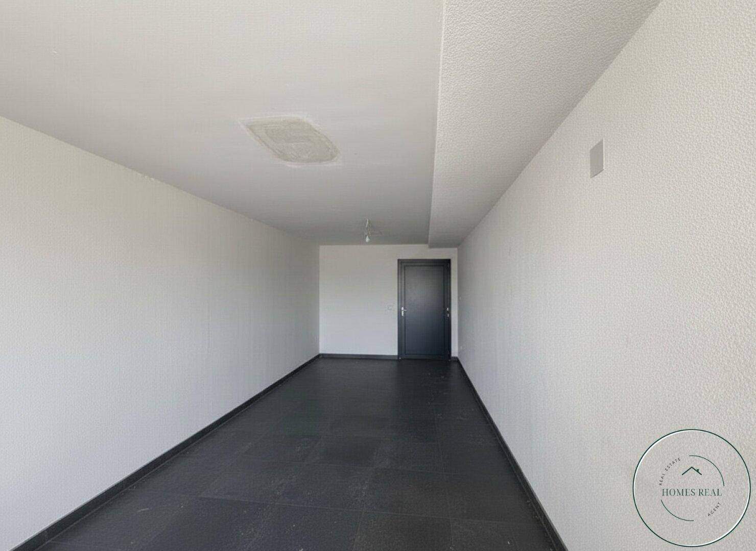 Leerer Raum mit dunklem Fliesenboden und weißen Wänden, bereit zur individuellen Gestaltung.