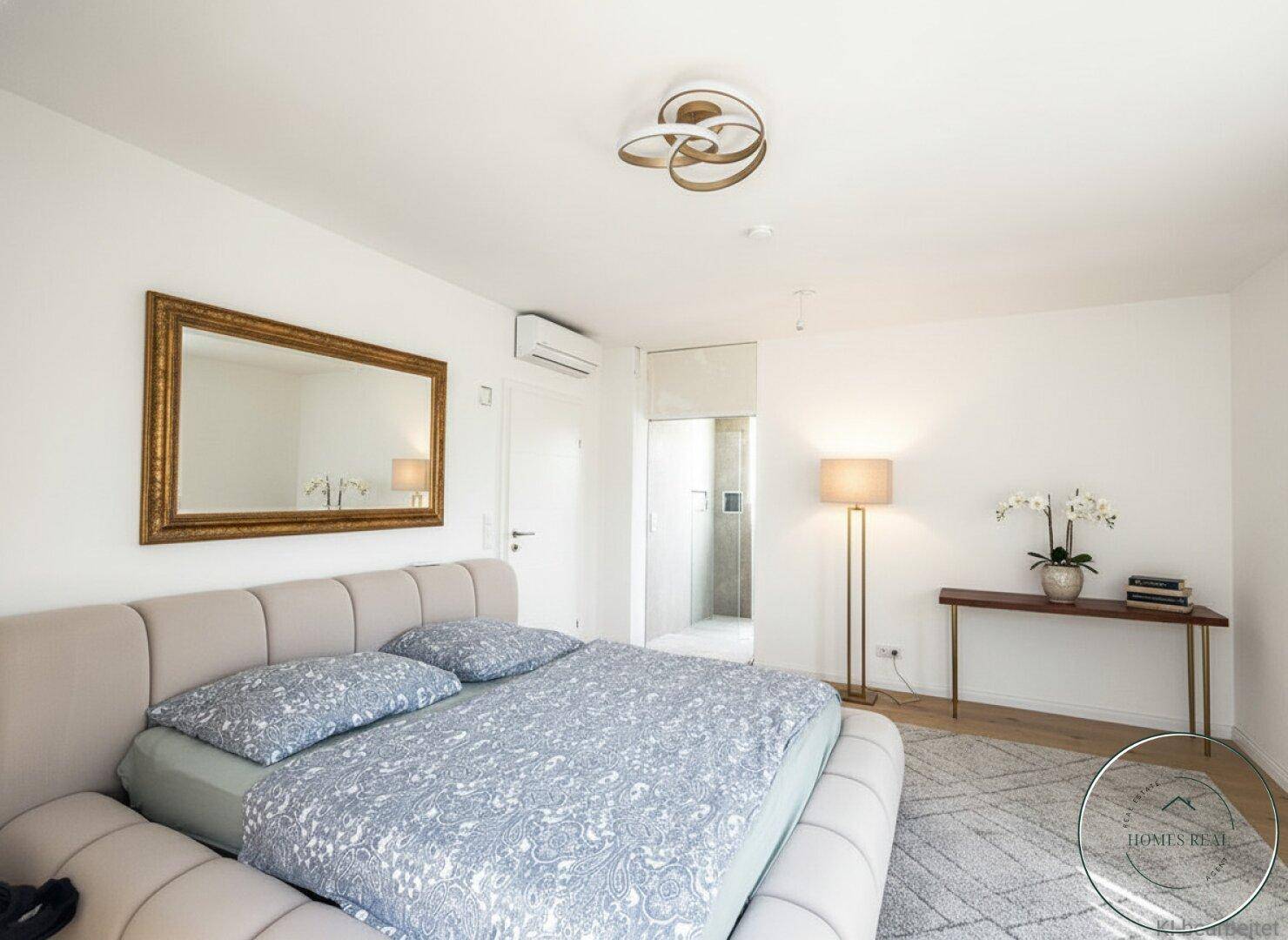 Geräumiges Schlafzimmer mit großem Bett, Spiegel, Holzboden und direktem Zugang zum Badezimmer.