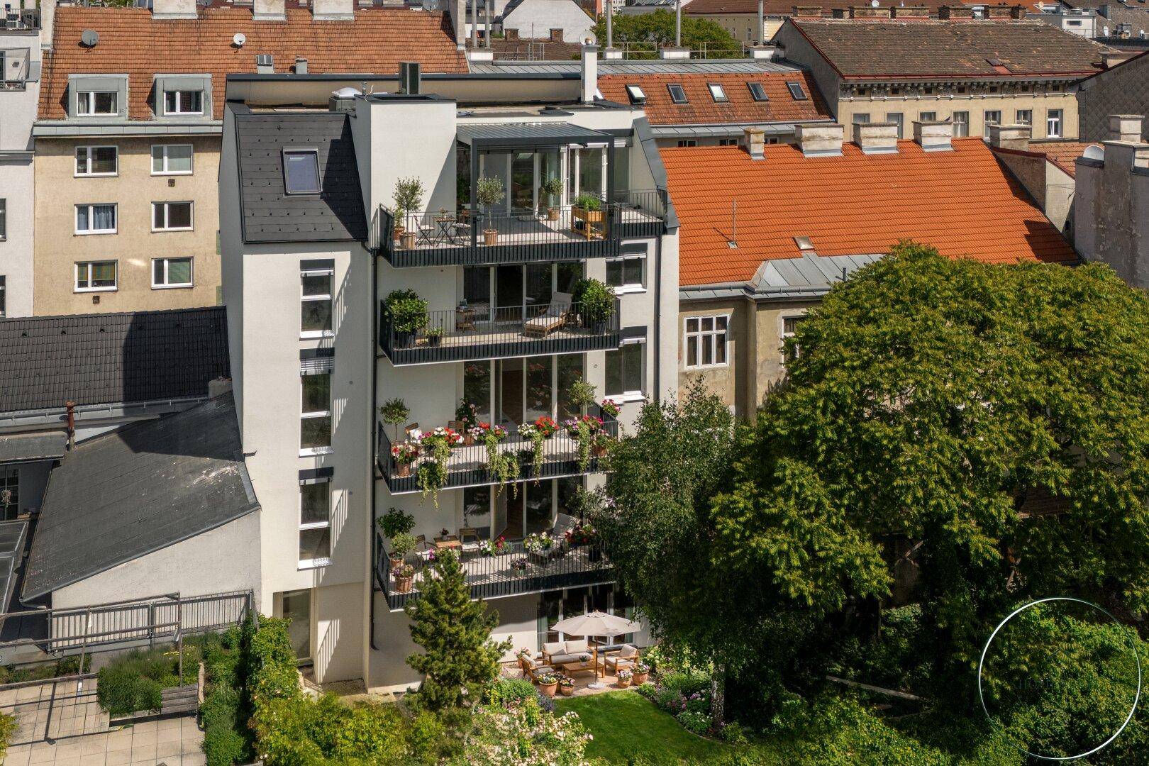 Luftaufnahme eines modernen Mehrfamilienhauses mit Balkonen und Dachterrasse in urbaner Umgebung.