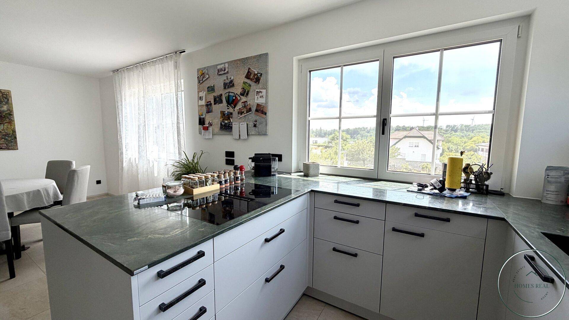 Moderne Küche mit Kücheninsel, grünen Arbeitsplatten und einem weiten Ausblick durch das große Fenster.