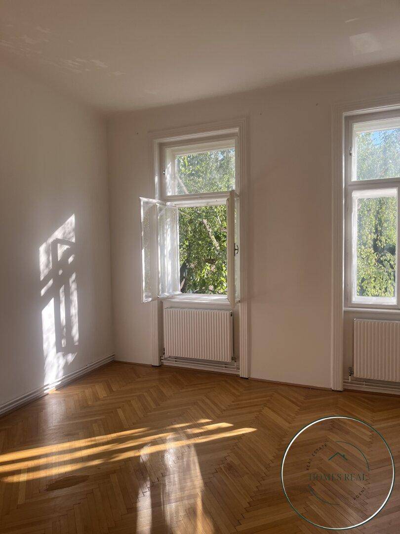 Unmöbliertes Schlafzimmer mit Fischgrätparkett, großen Fenstern und viel Sonnenlicht.