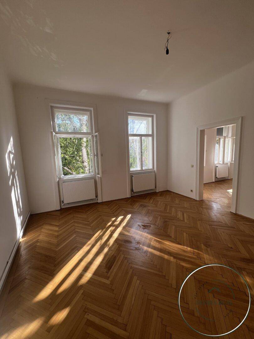 Geräumiges, unmöbliertes Wohnzimmer mit Fischgrätparkett und viel Tageslicht.