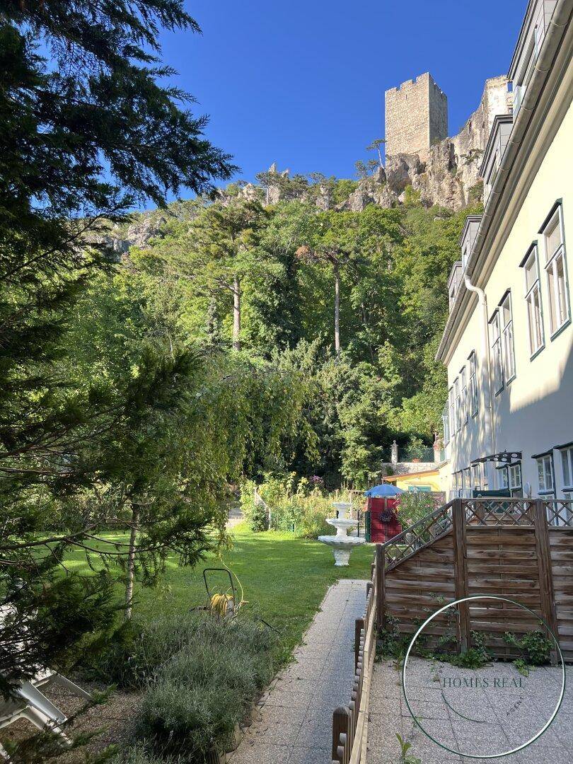 Seitenansicht des Gebäudes mit Garten und Blick auf die bewaldete Berglandschaft.
