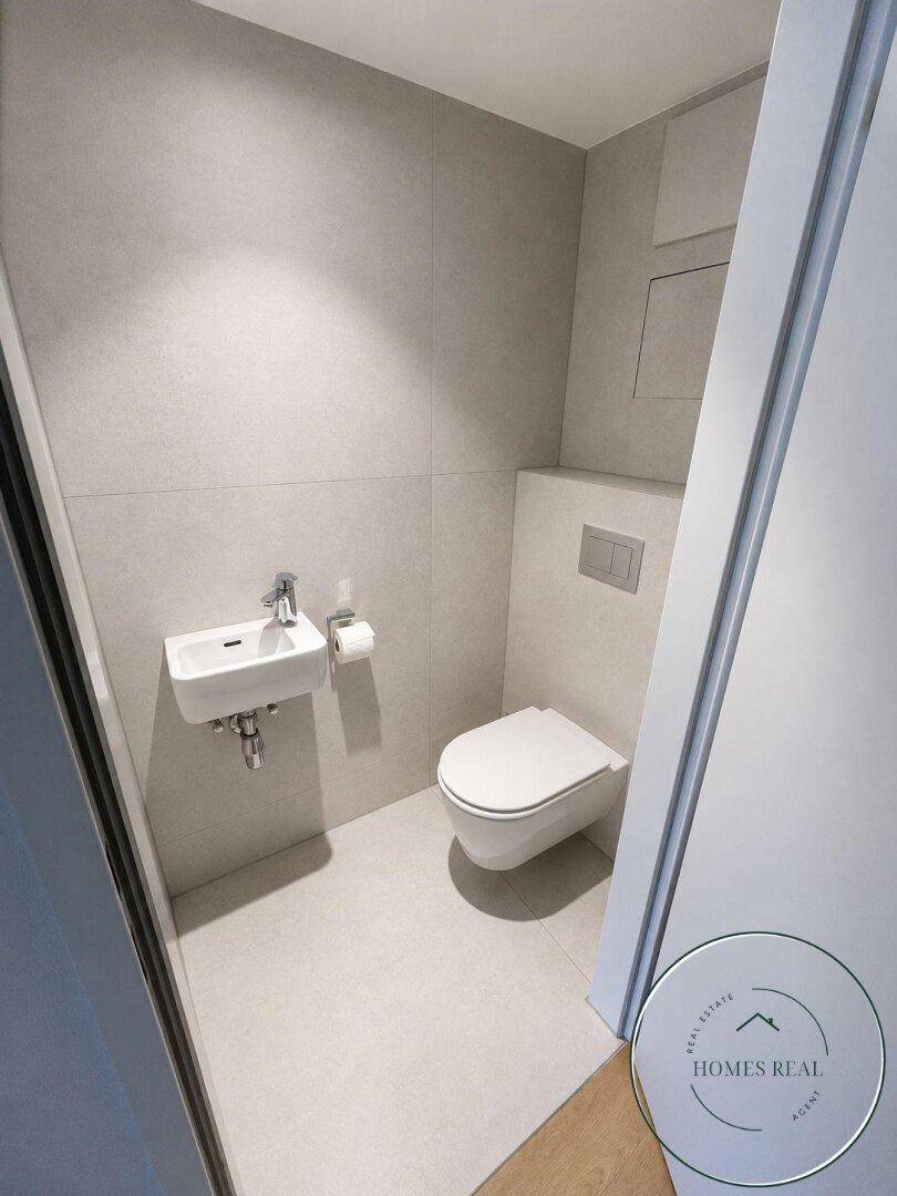 Modernes Gäste-WC mit wandhängender Toilette und kleinem Waschbecken, in hellen Farbtönen gehalten.