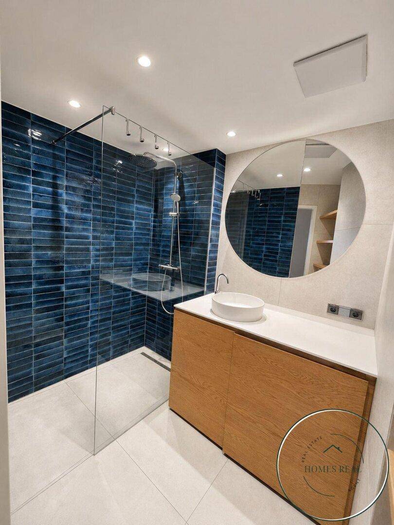 Elegantes Badezimmer mit großer begehbarer Dusche, blauen Fliesen und modernem Waschtisch.