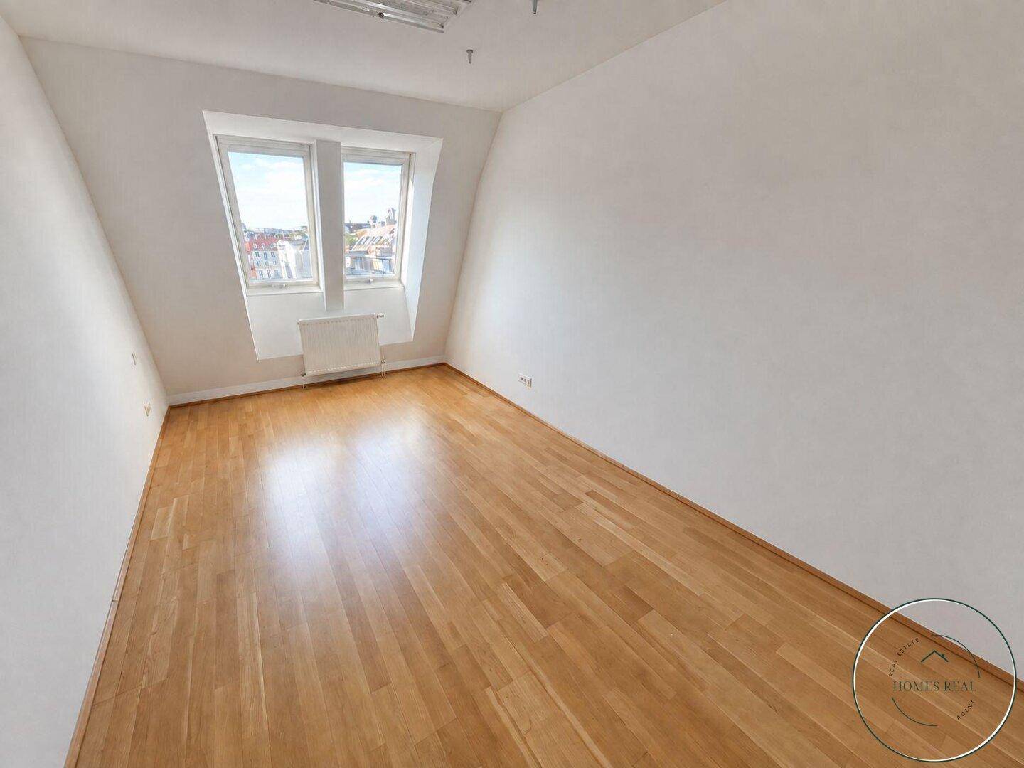 Leeres Arbeitszimmer mit Holzboden und Dachfenstern, bietet eine helle und ruhige Arbeitsumgebung.