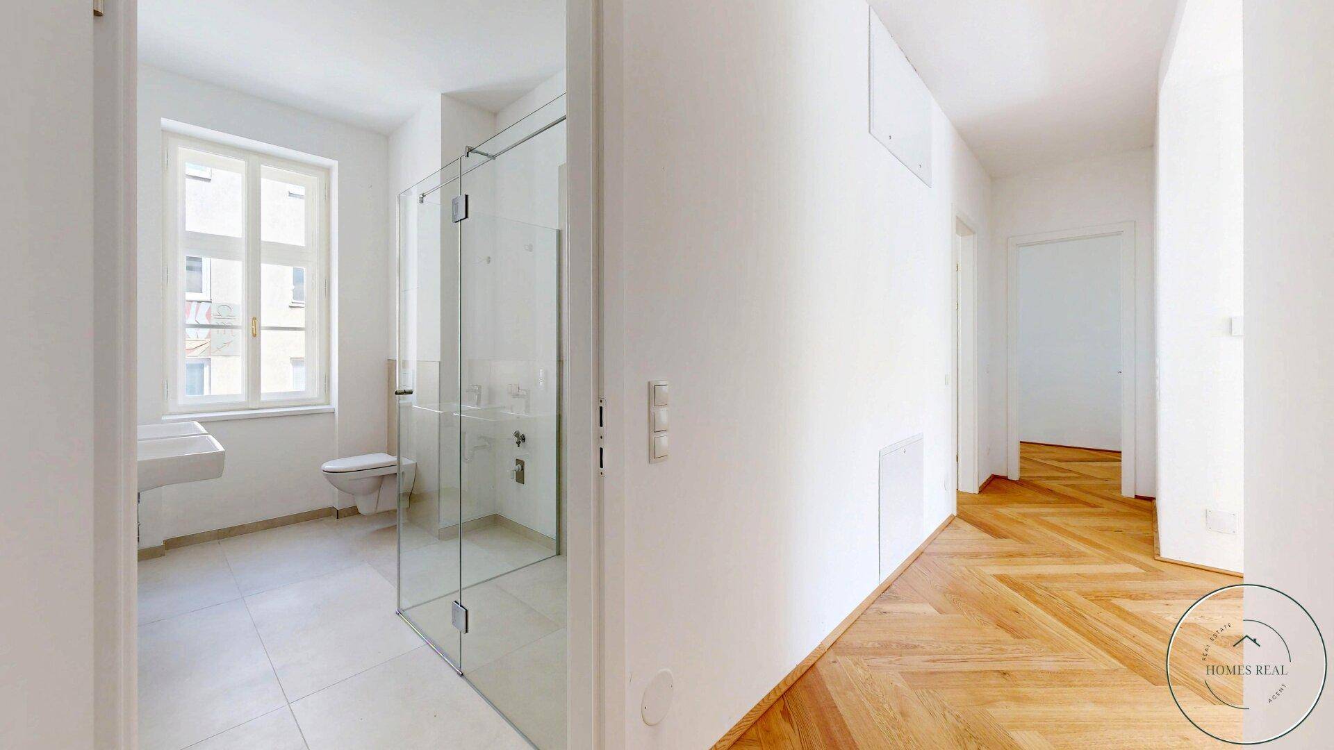 Modernes Badezimmer mit ebenerdiger Glasdusche, Wand-WC und hellem Fliesenboden.
